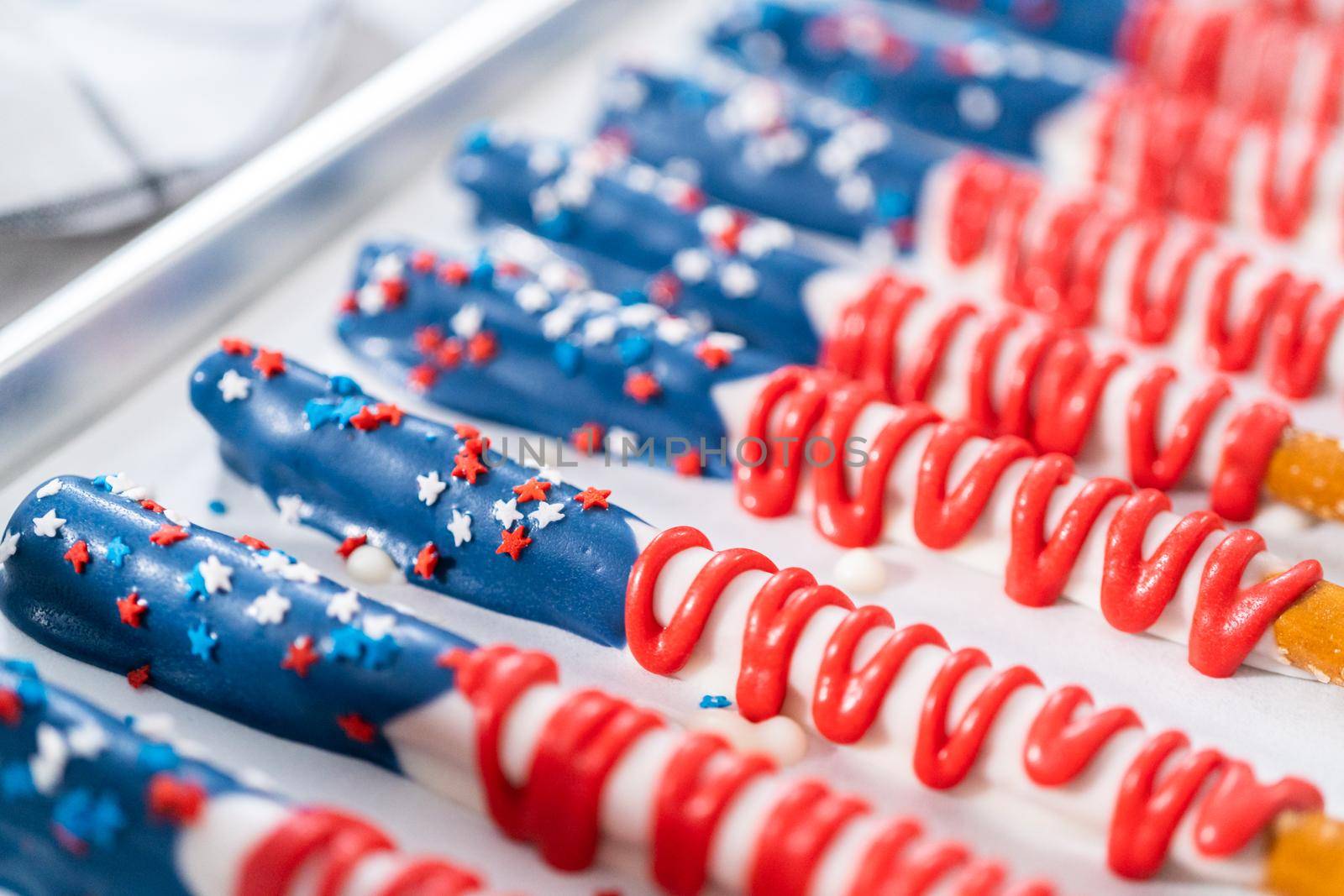 Homemade chocolate-covered pretzel rods decorated like the American flag drying on a baking sheet lined with parchment paper.