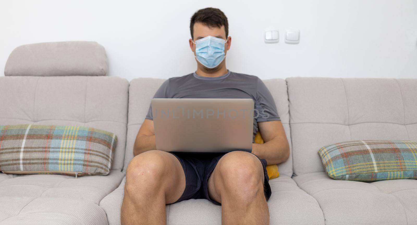 mask covering whole face man with laptop on sofa by Chechotkin