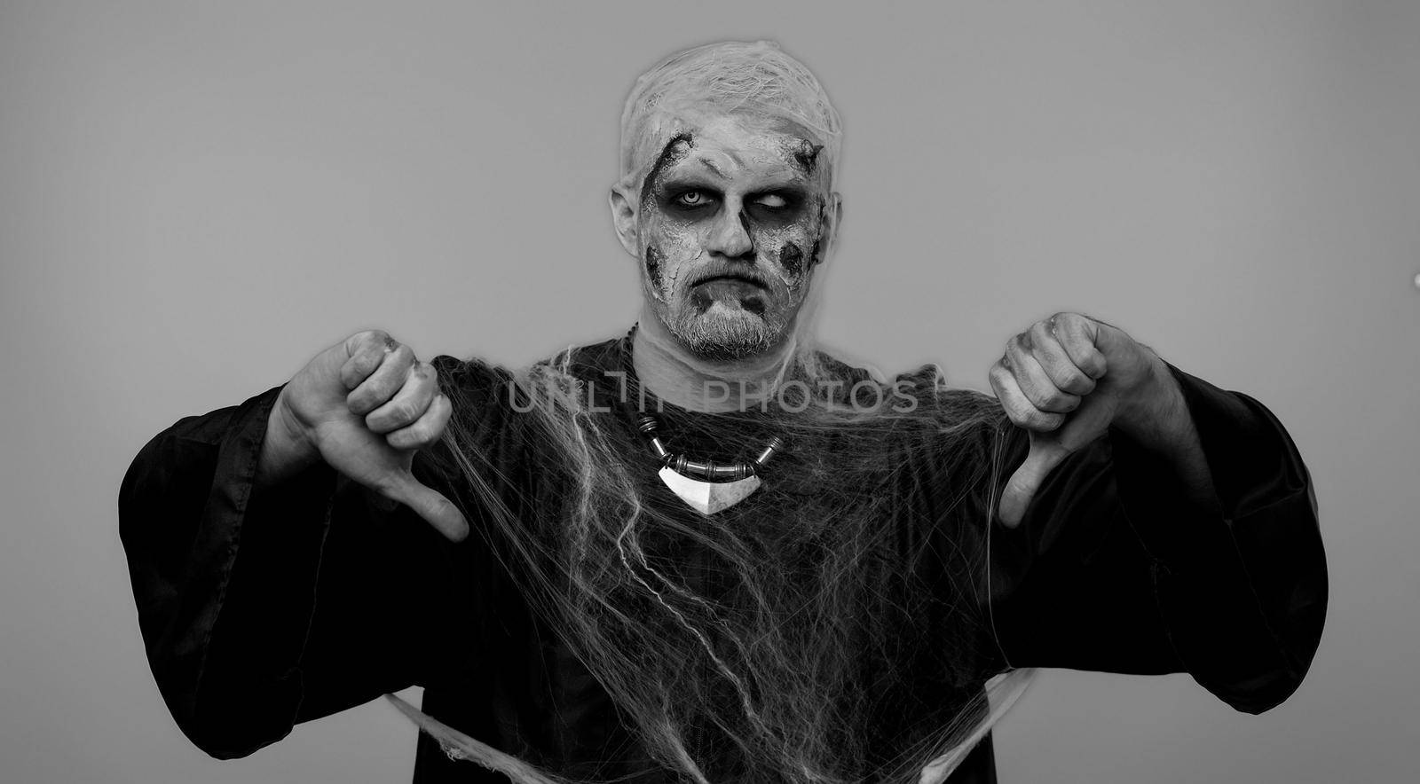 Scary man in carnival costume of Halloween crazy zombie undead with bloody wounded scars face showing thumbs down sign gesture, expressing discontent, disapproval, dissatisfied, dislike. Chroma key