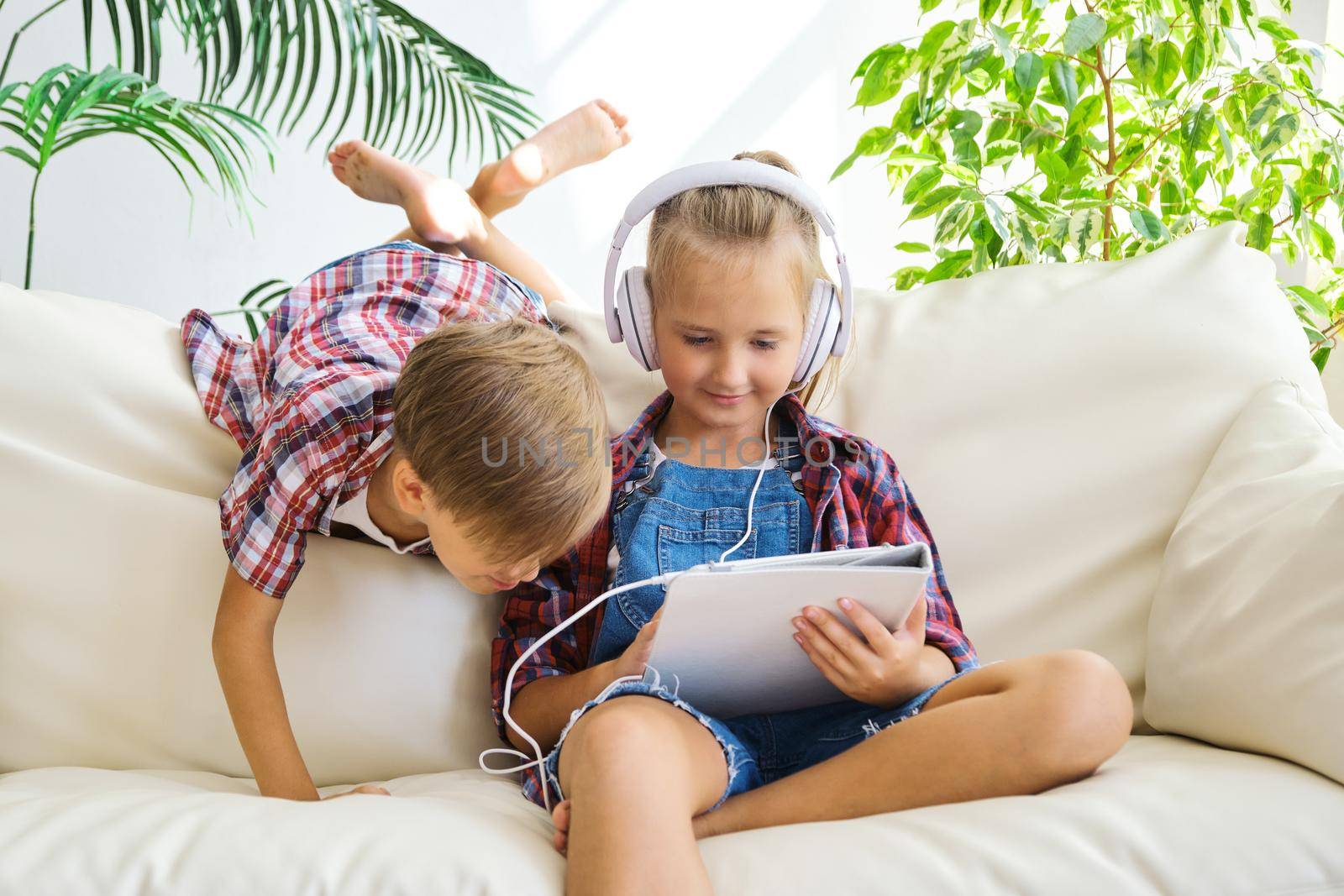 Cute brother and sister with headphones enjoying tablet at home. family, children, technology and home concept