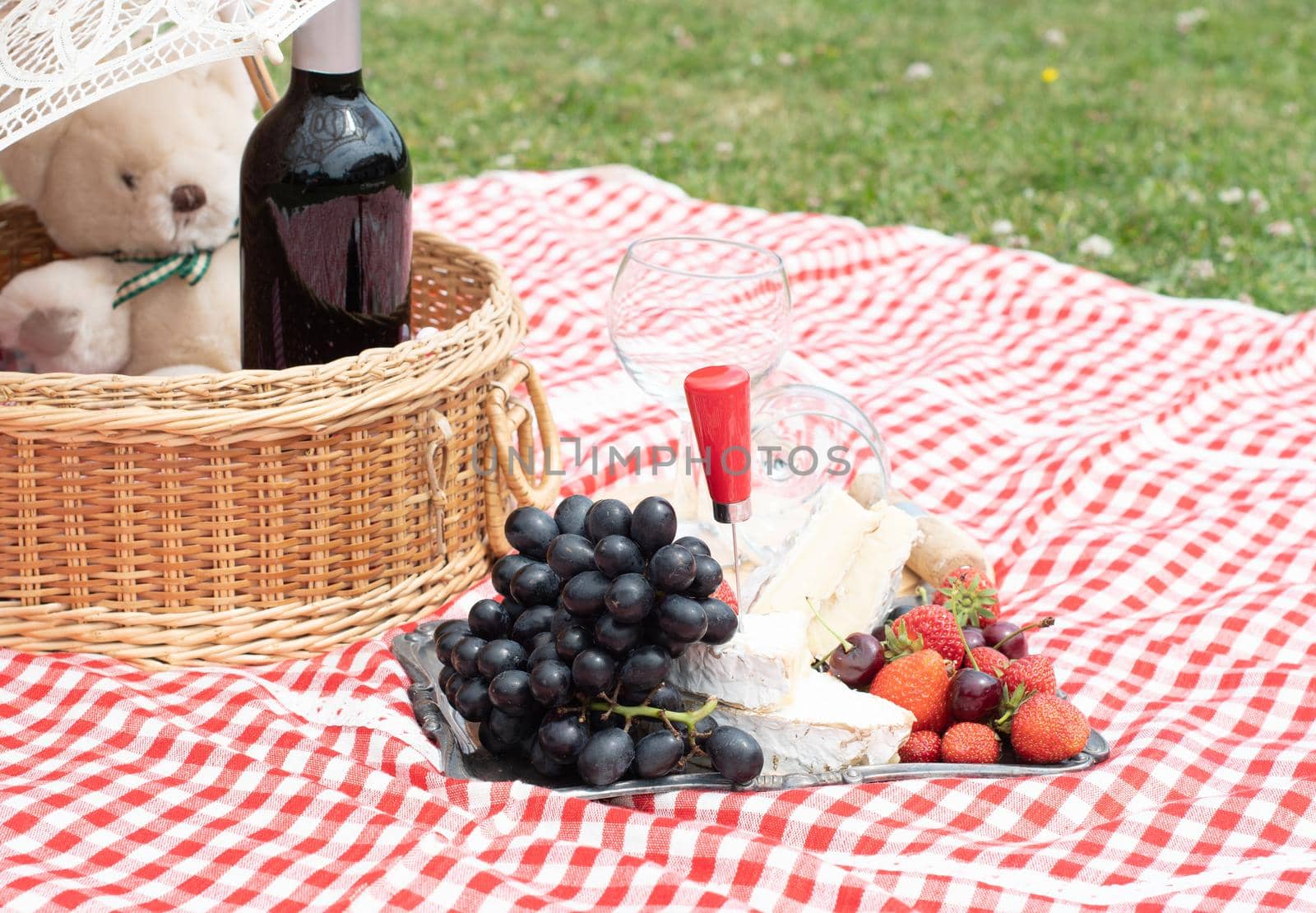 summer picnic on a green lawn with red wine, cheese and fresh berries, grapes, cherries, strawberries, summer vacation. High quality photo