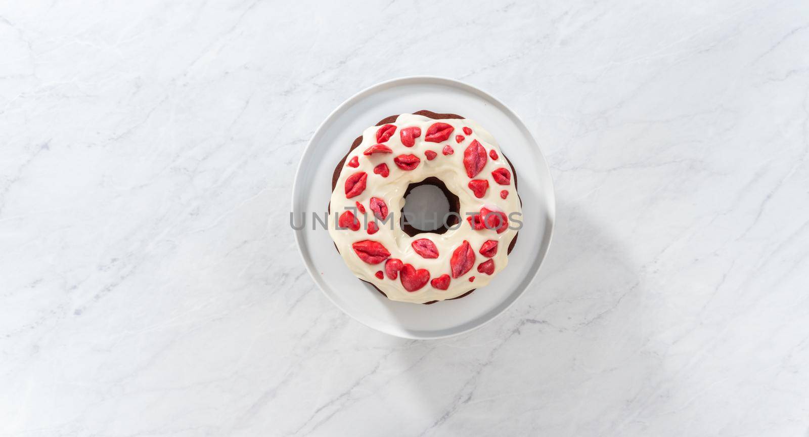 Flat lay. Decorating red velvet bundt cake with chocolate lips and hearts over cream cheese glaze.