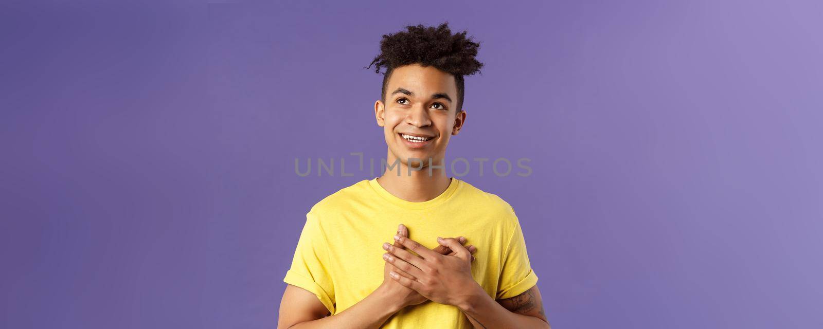 Close-up portrait of touched, romantic attractive man, hold hands on heart, remember nice lovely memory, looking up daydreaming, smiling pleased, appreciate something, purple background by Benzoix