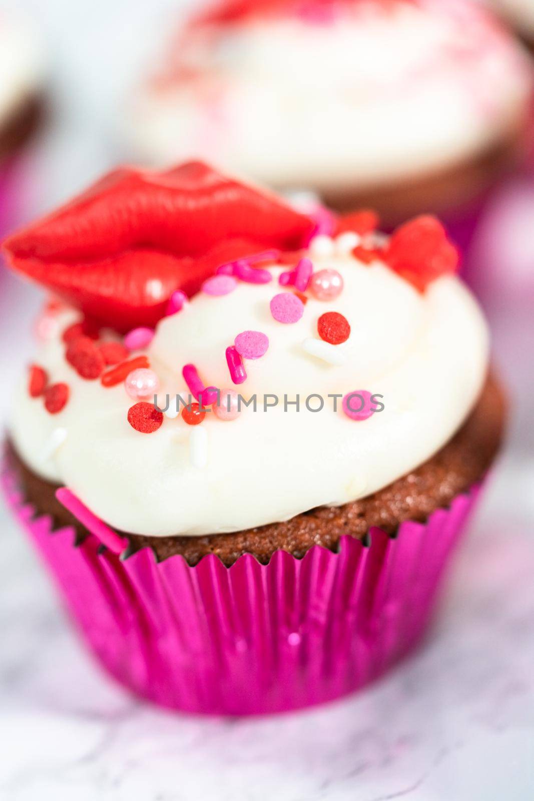 Red velvet cupcakes with cream cheese frosting and decorates with heart and kiss shaped red chocolates.