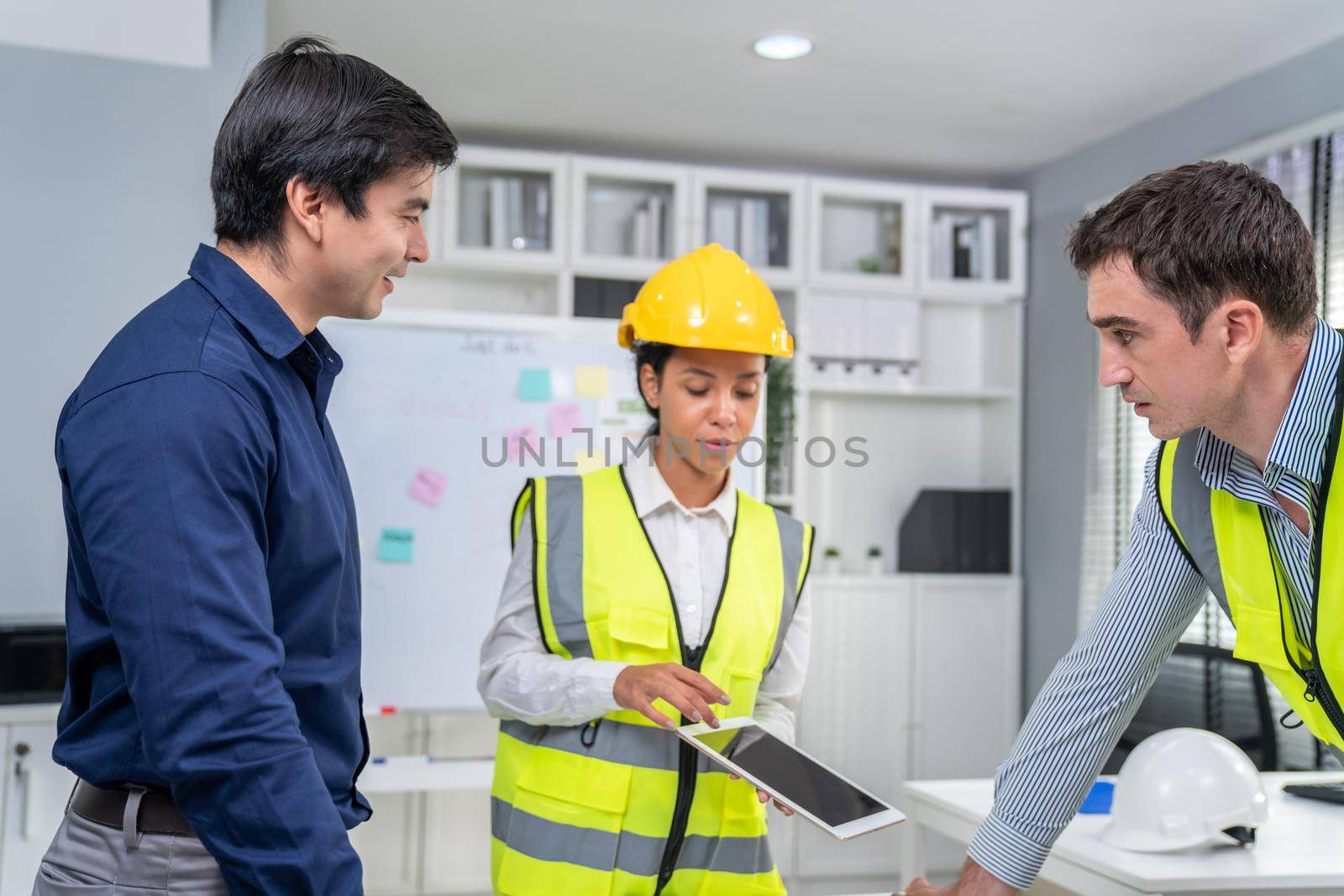 Engineers and competent employer discussing plans and blueprints together with tablet in the office. Concept of team contribution of ideas for engineering project.