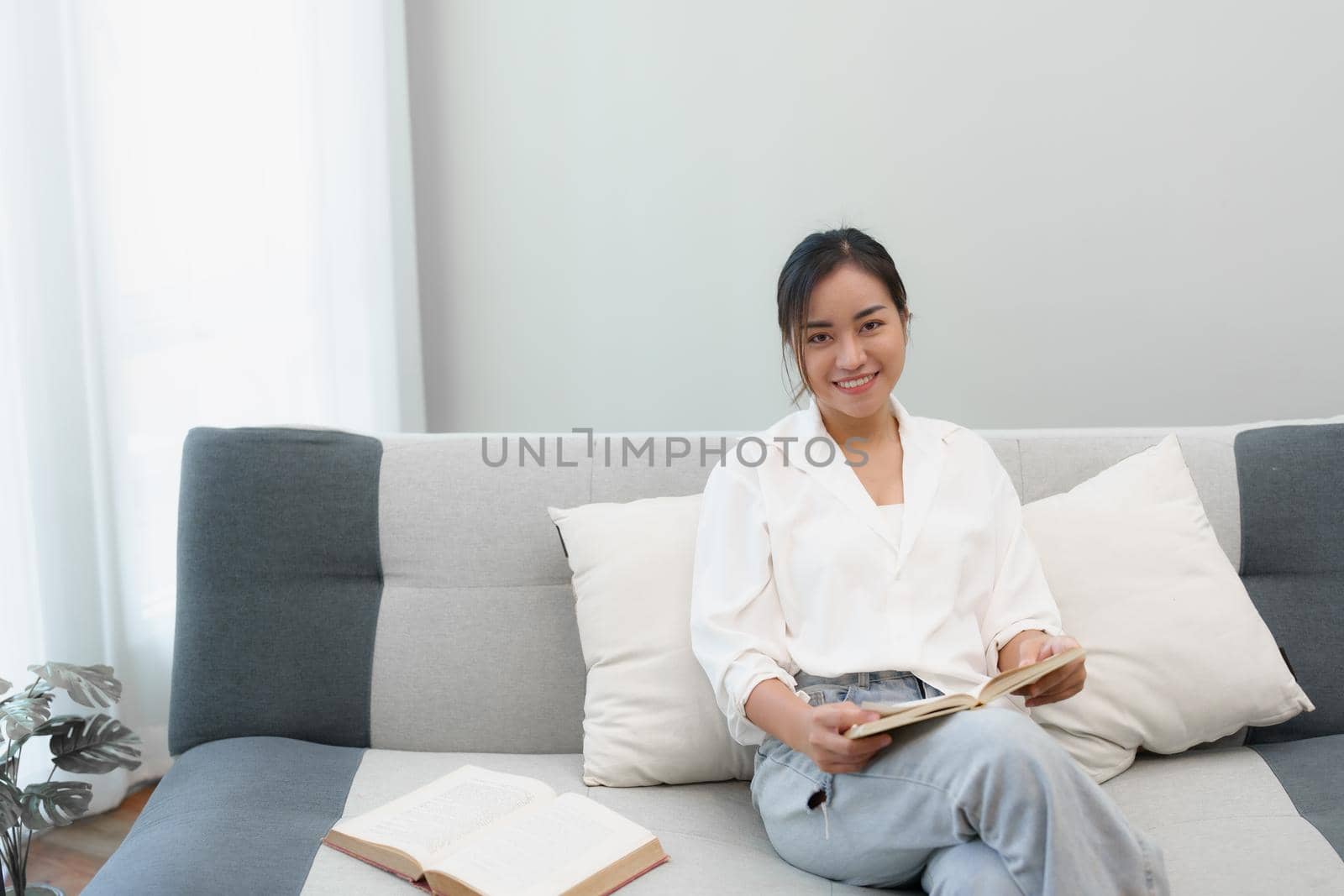 Portrait of a young Asian woman reading a book on the sofa to relax.