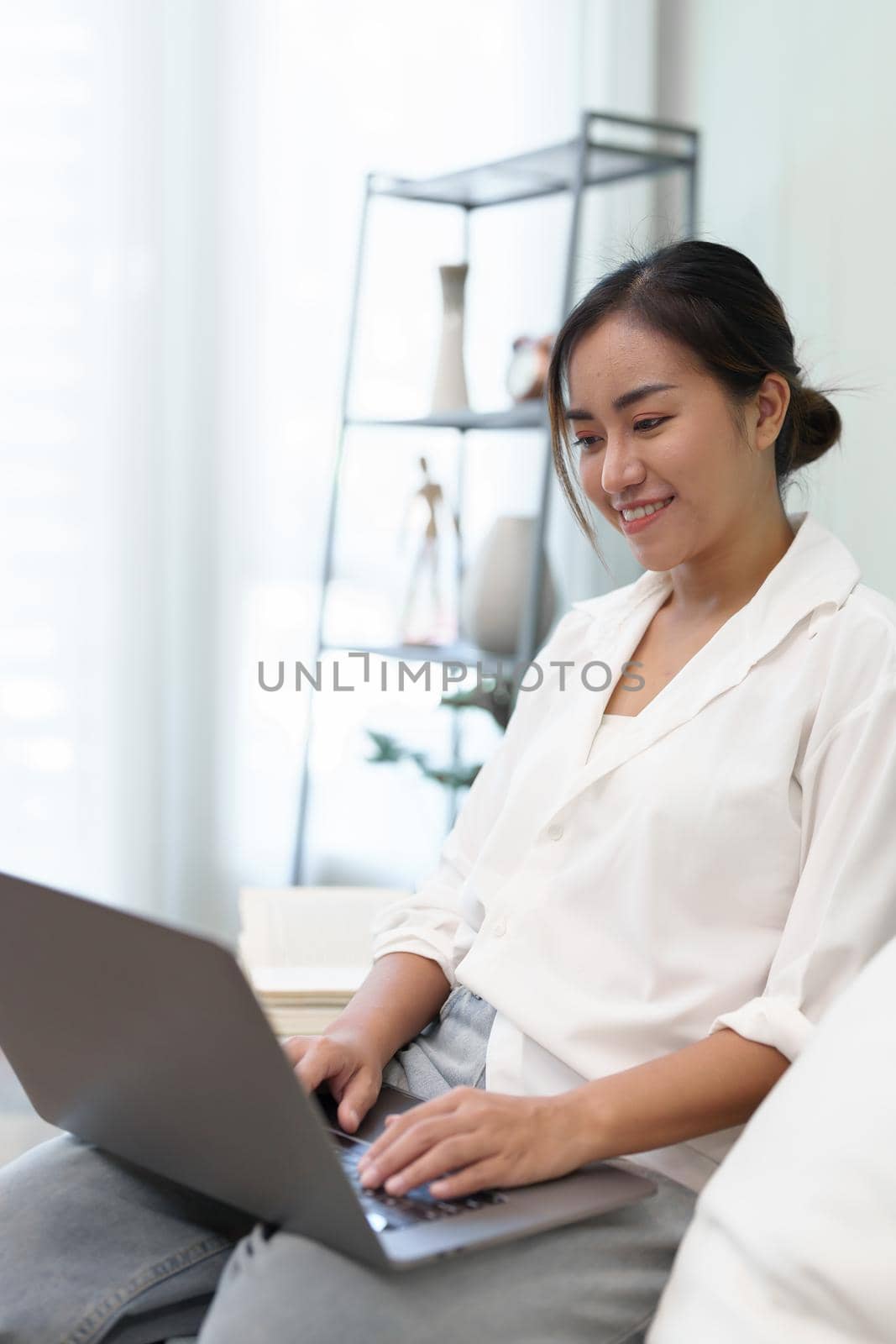 Portrait of a young Asian woman sitting on the sofa using a computer. by Manastrong