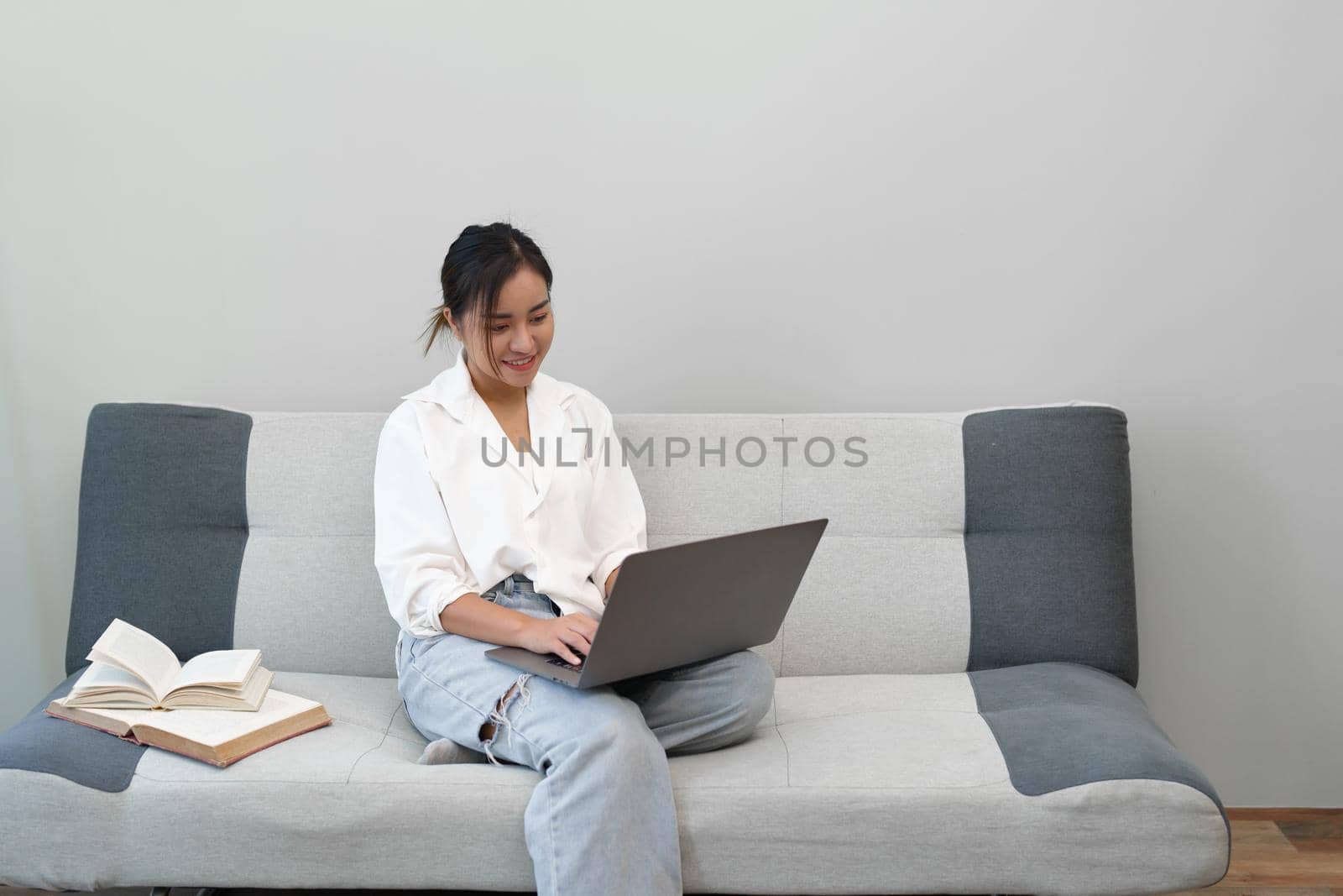 Portrait of a young Asian woman sitting on the sofa using a computer. by Manastrong
