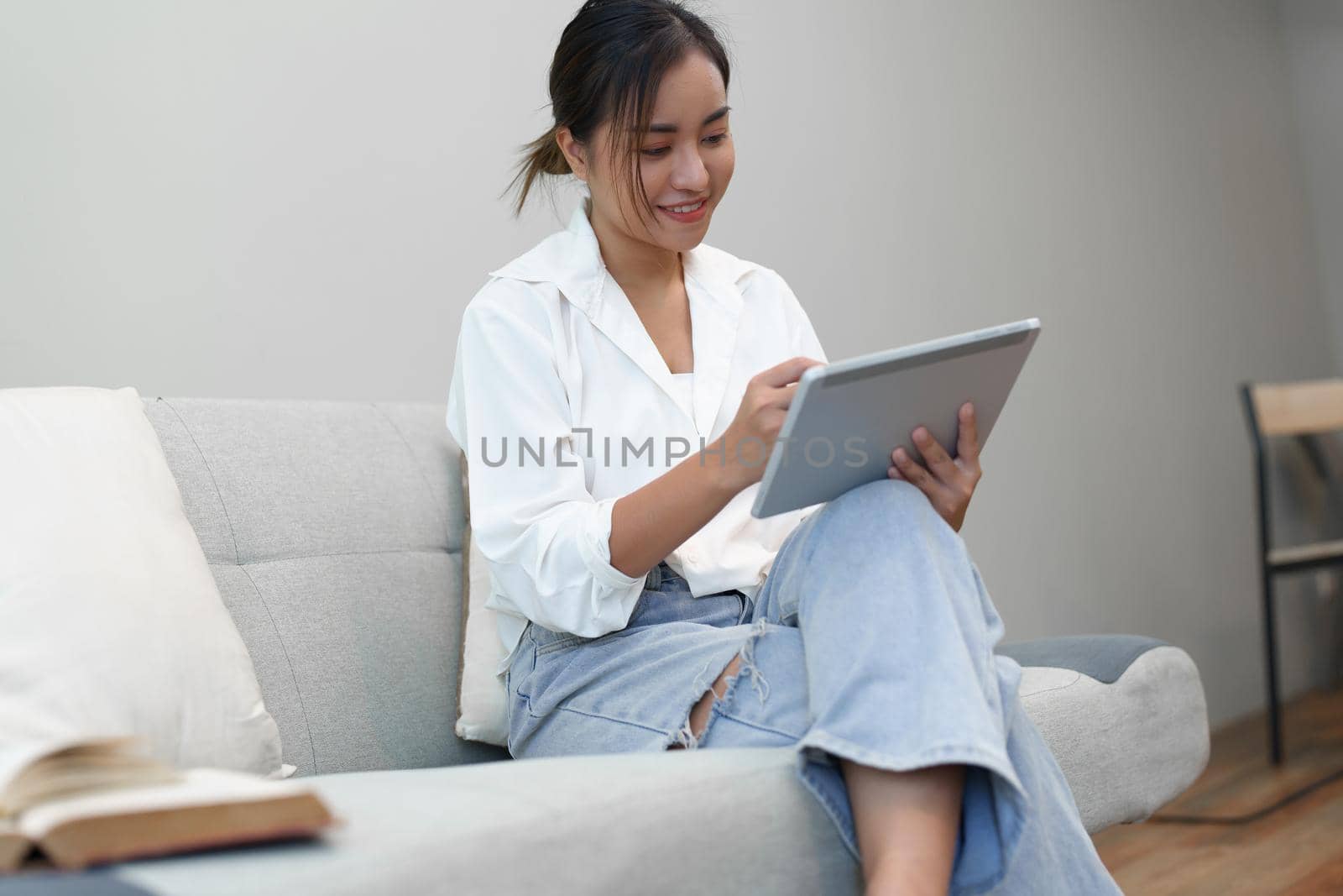 Portrait of a young Asian woman sitting on the sofa using a tablet. by Manastrong