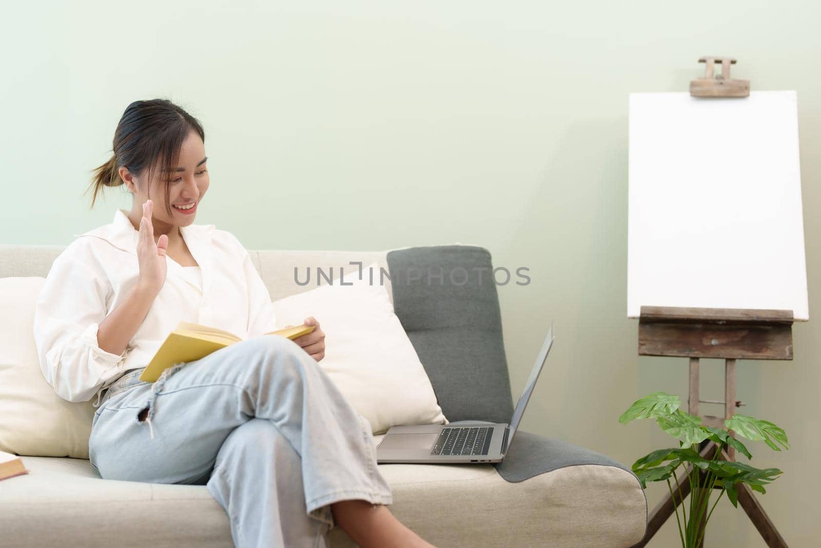 Portrait of a young Asian woman reading a book on the sofa to relax.