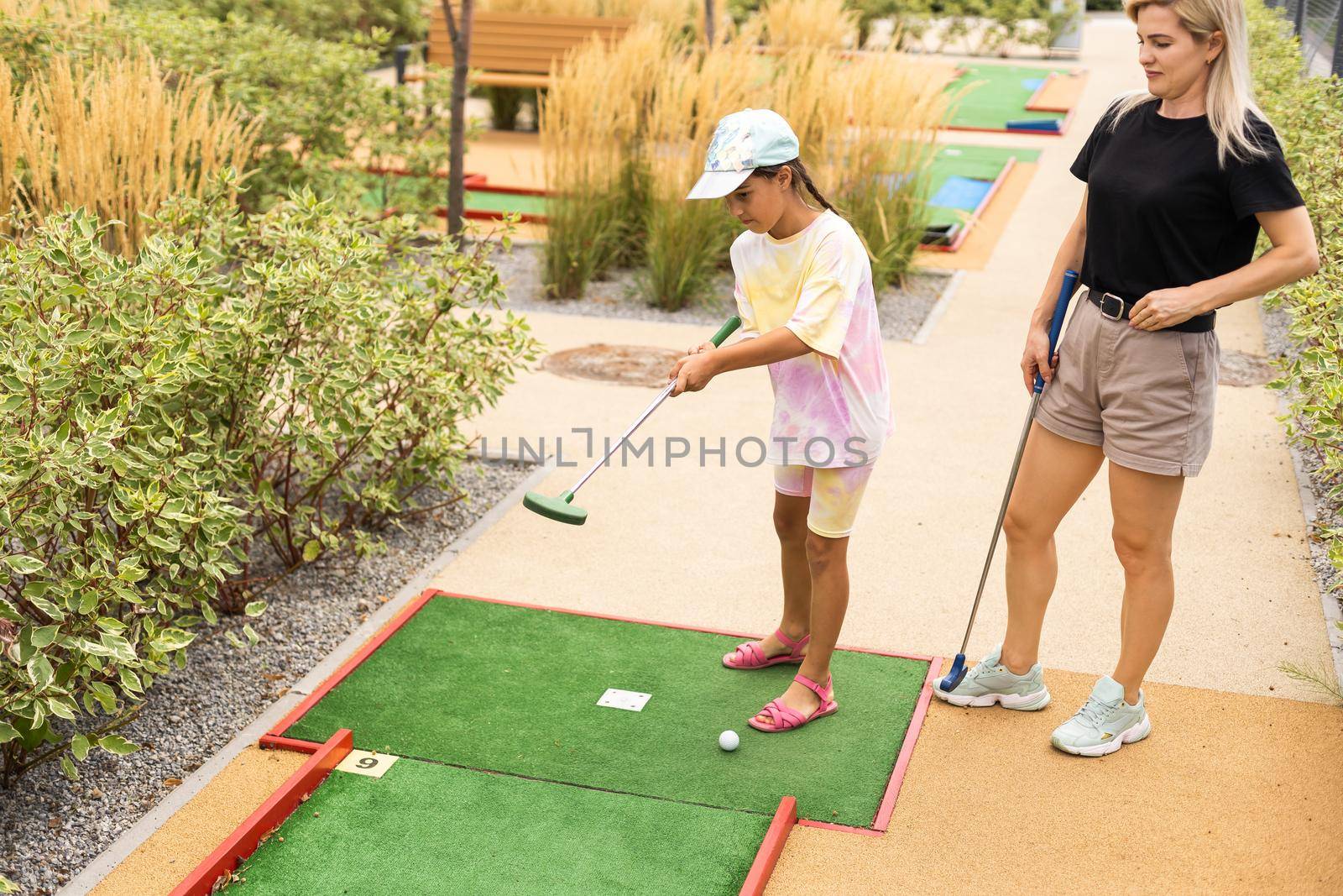 mother and daughter playing mini golf, children enjoying summer vacation.