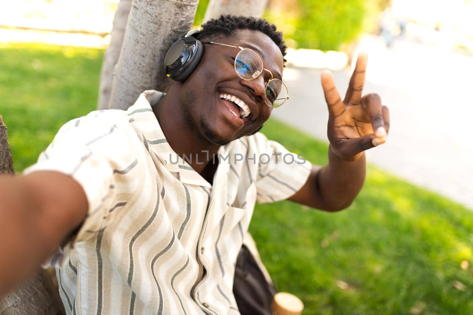 Black male teenager with glasses taking selfie on campus. Smiling, happy, African american college student looking at camera outdoors. Copy space. Technology.