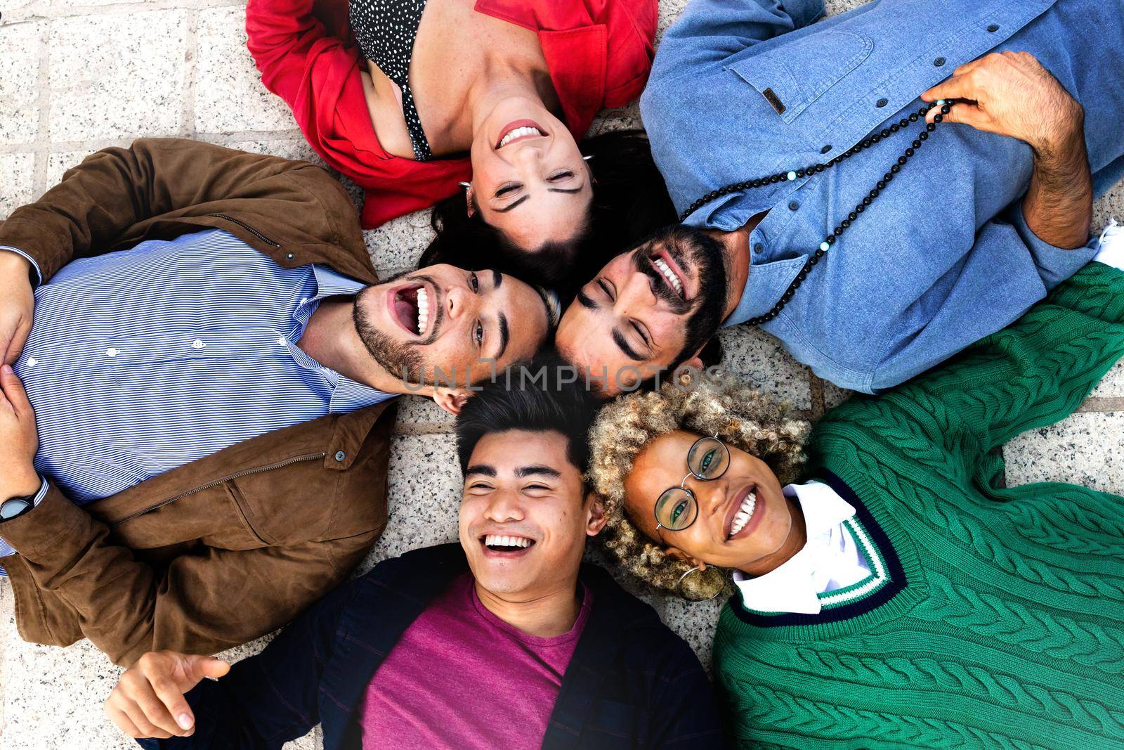 Happy multiracial friends lying down with heads touching forming a circle. by Hoverstock
