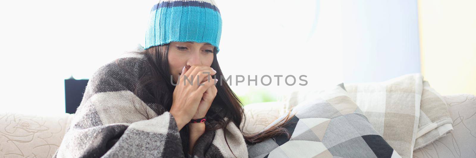 Sick woman in hat sitting under blanket at home by kuprevich