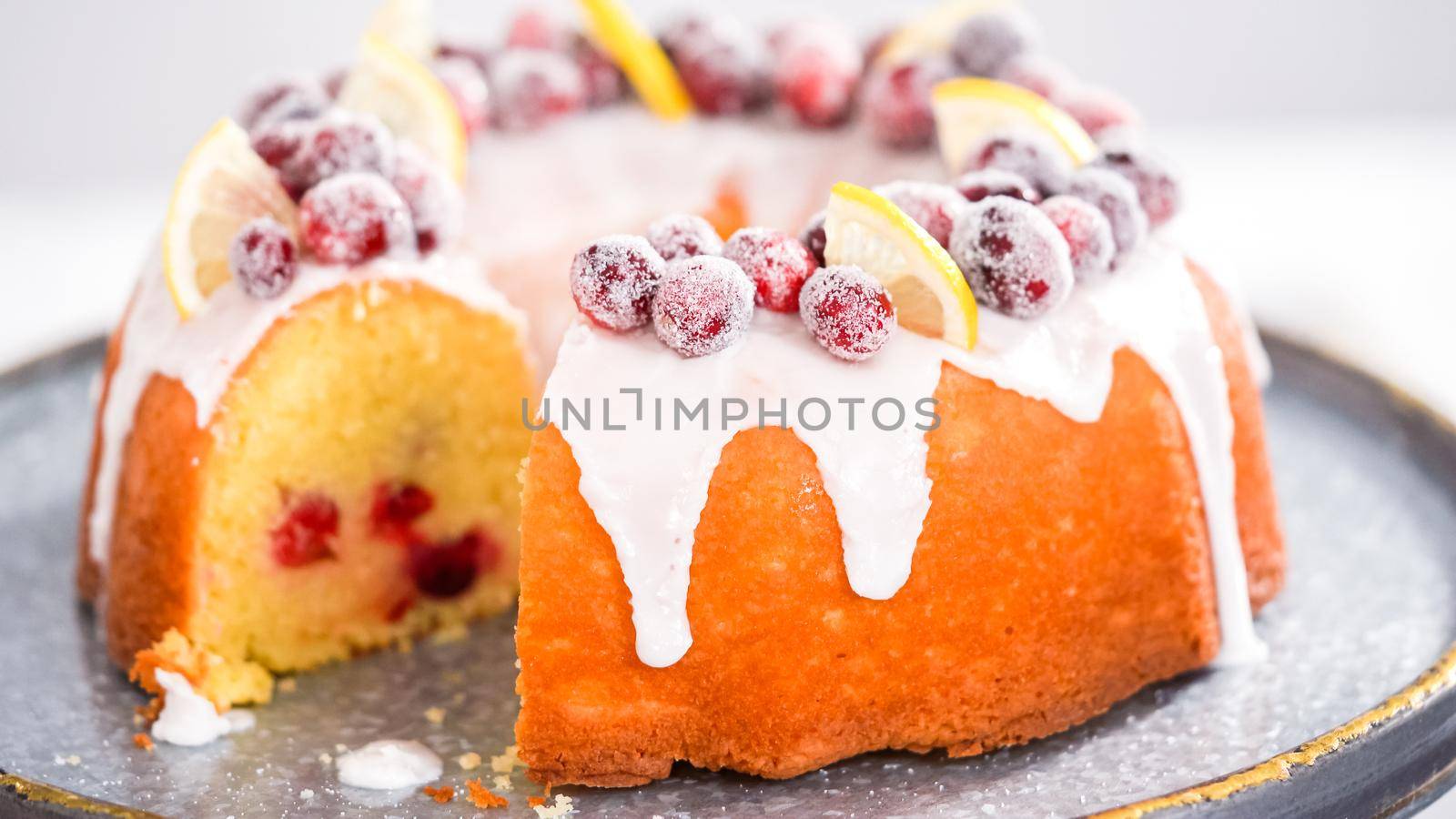 Step by step. Slicing lemon cranberry bundt cake decorated with sugar cranberries and lemon wedges.