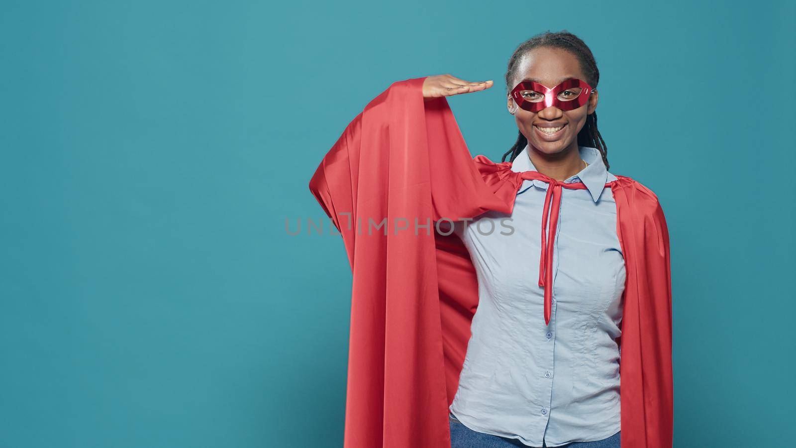 Portrait of superhero with cape and red mask doing army military salute on camera. Posing as cartoon character with hero costume to show respect, feeling cofident and powerful.