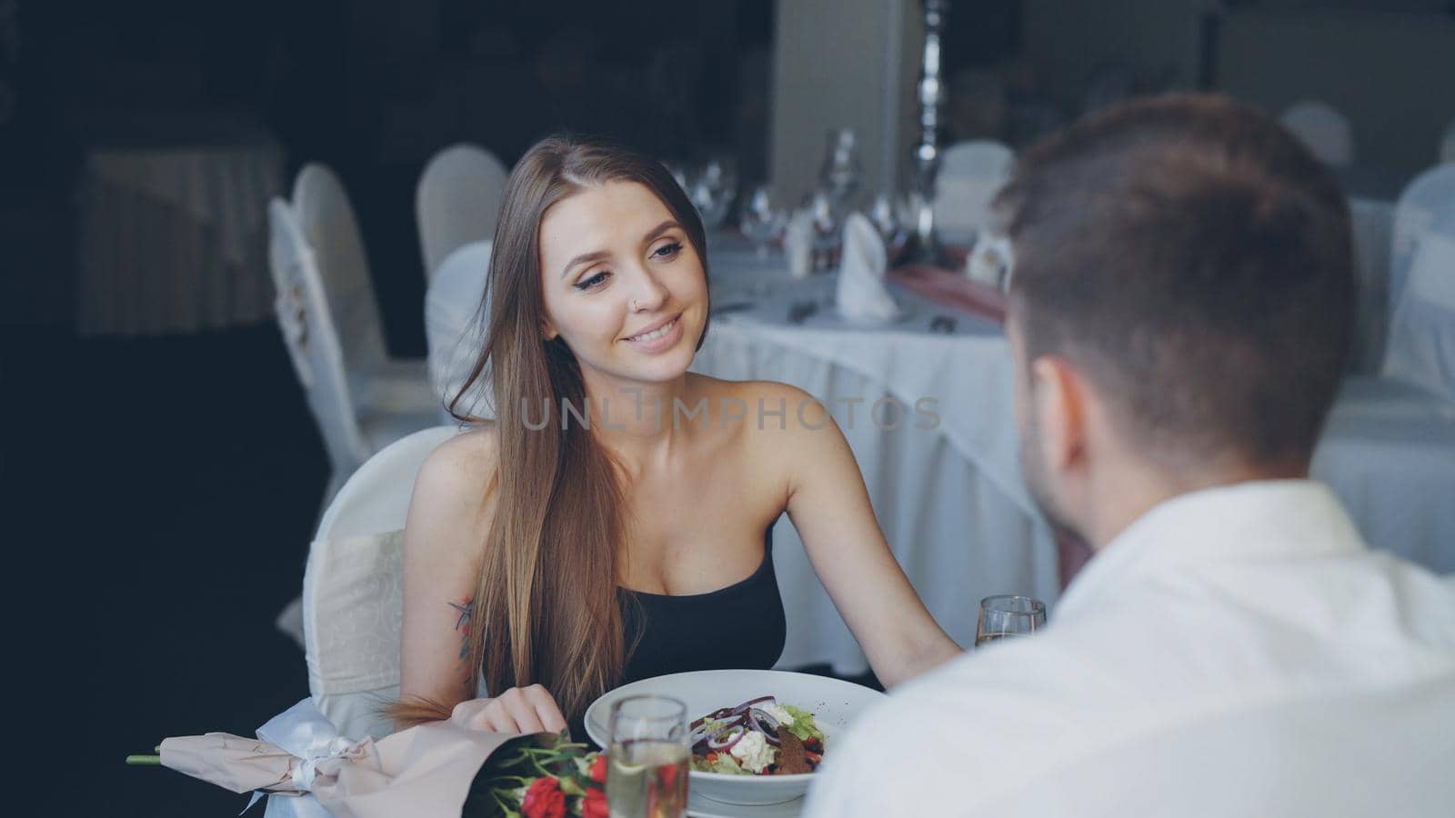 Attractive girlfriend and boyfriend in fance clothing are clinking glasses, drinking champagne and talking on romantic date in classy restaurant. Romance, love and fine dining concept.