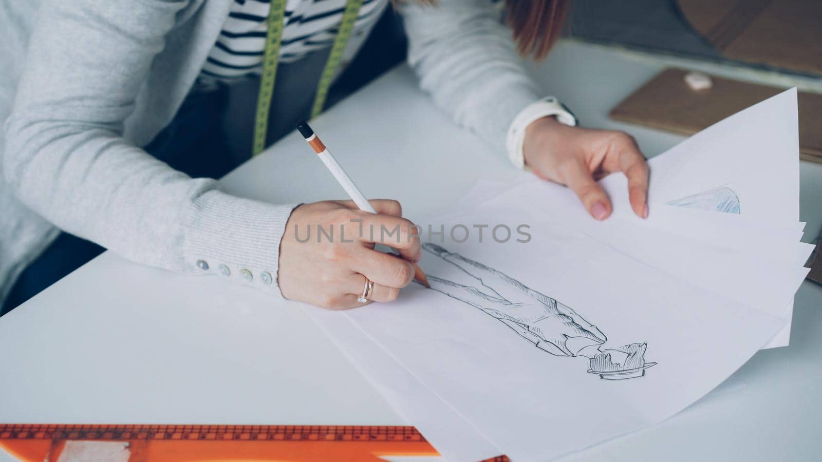 Close-up of fashion designer is drawing lines on clothing sketch. Woman is busy and concentrated on work.