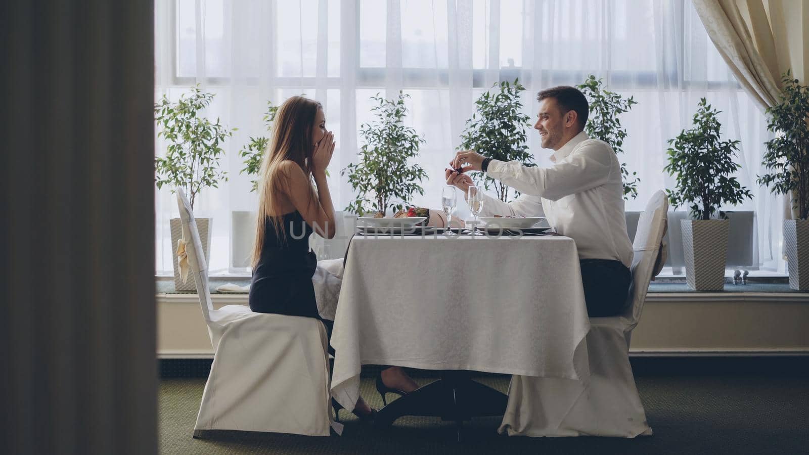 Marriage proposal of young good-looking man to pretty young lady during date in restaurant