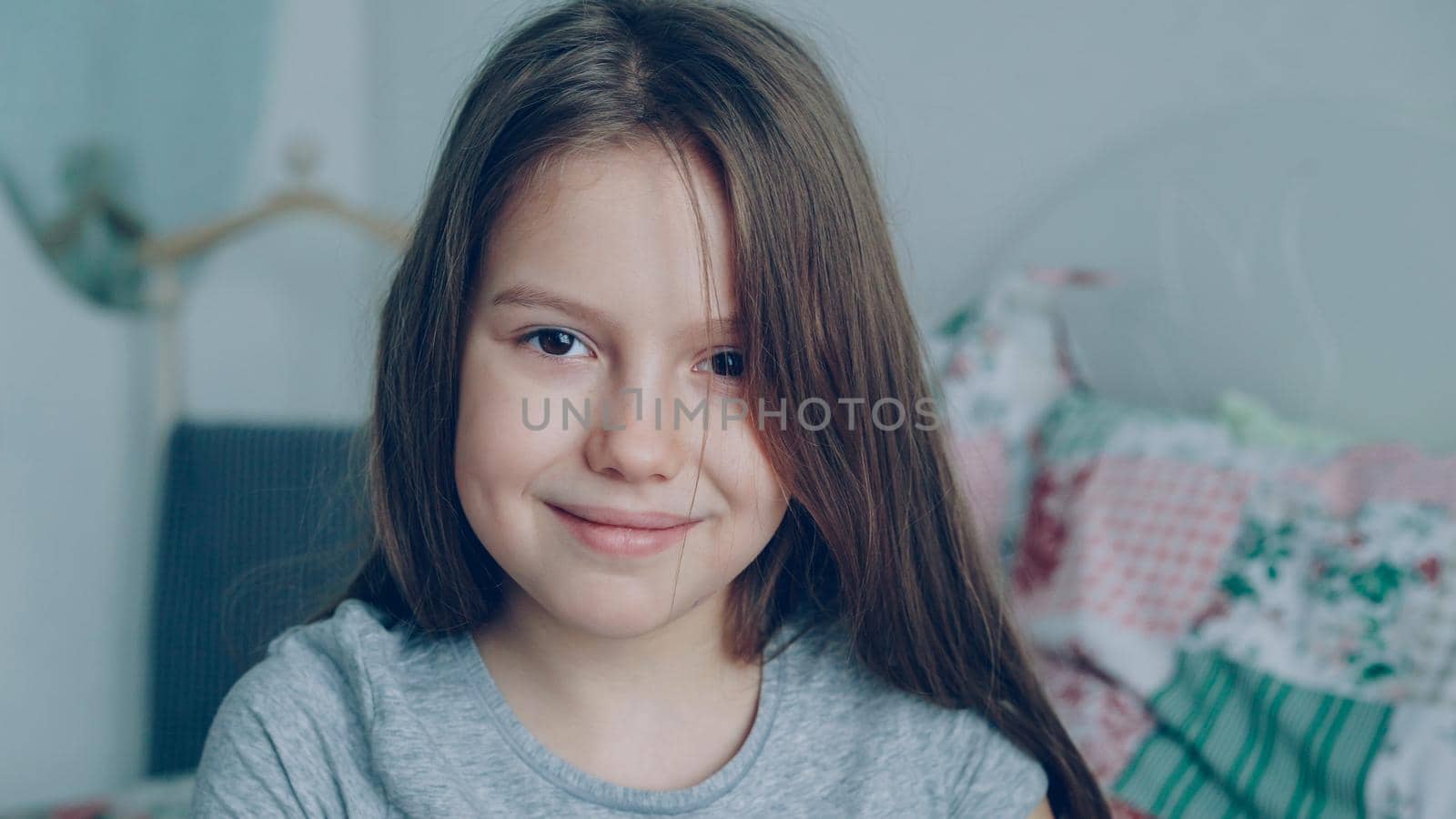 Close-up portrait of little cute girl looking at the camera and smiling kindly in cozy bedroom at home