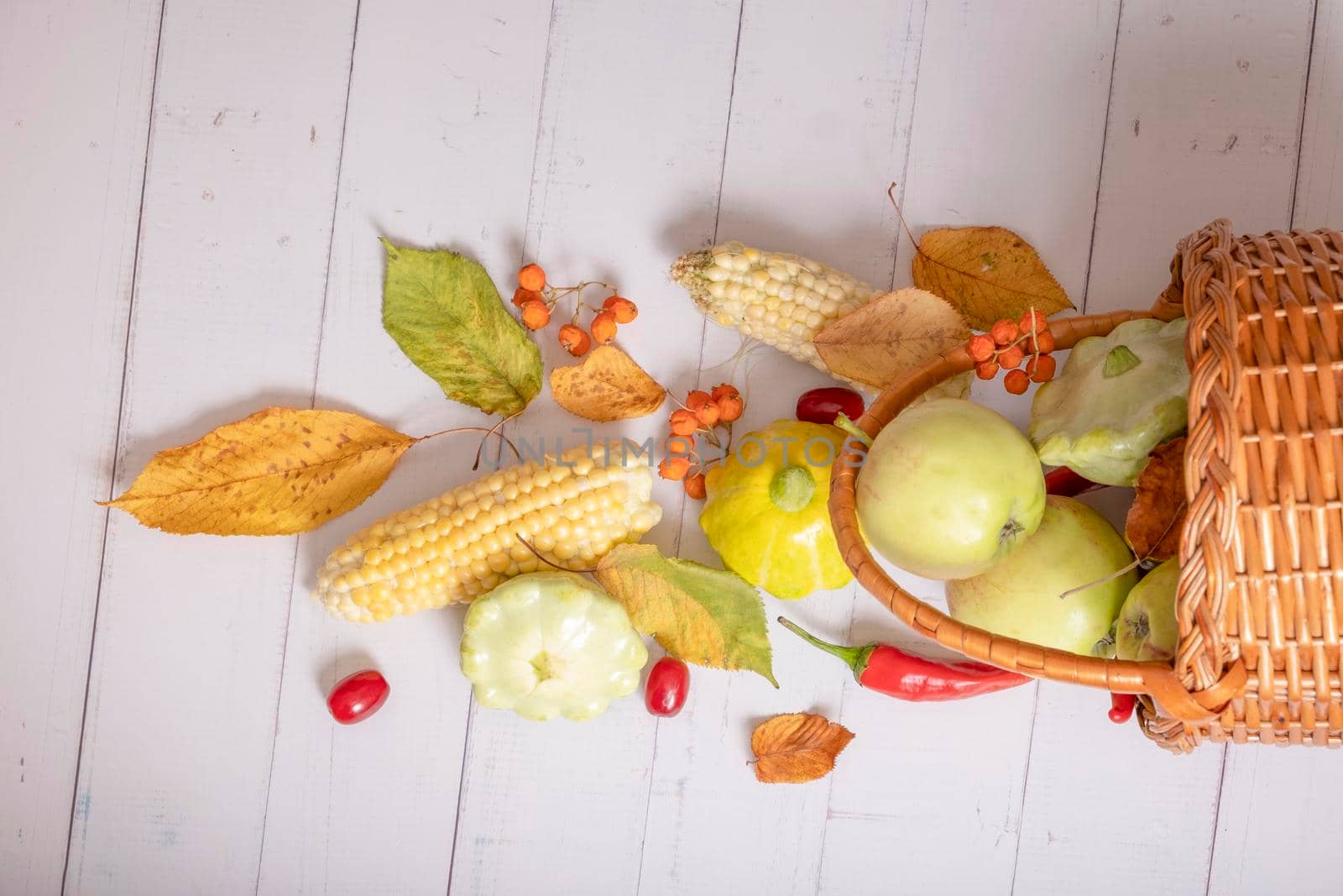 Top view autumn harvest basket with corn, apples, zucchini and peppers on a wooden background decorated with autumn leaves