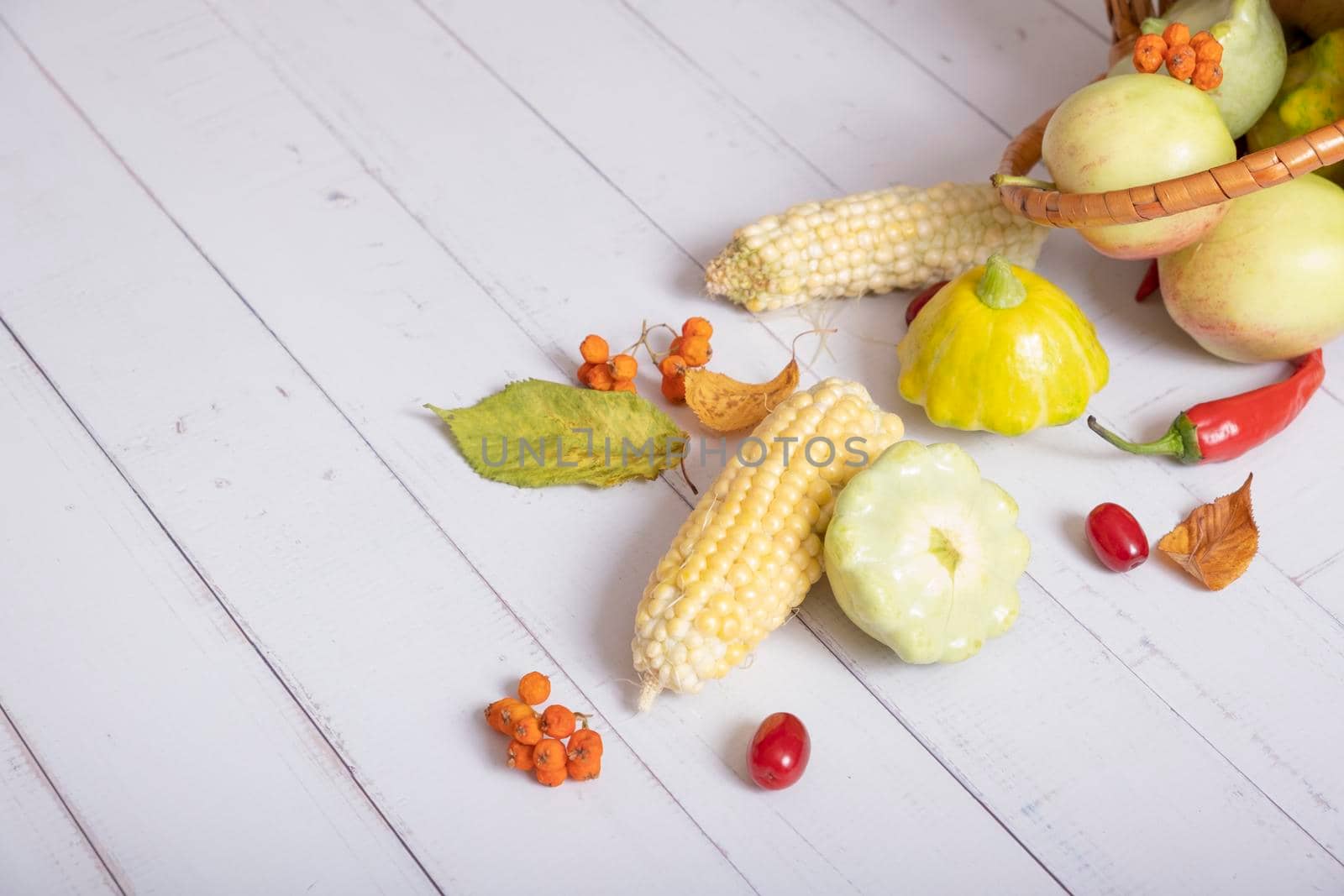 Fragment of autumn harvest basket with corn, apples, zucchini and peppers on a wooden background decorated with autumn leaves