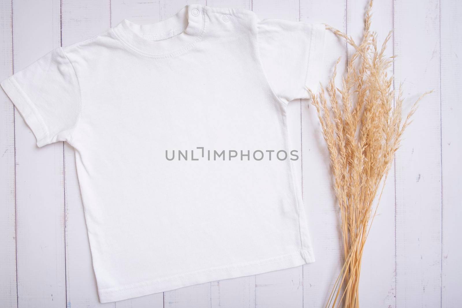 White children's t-shirt mockup for logo, text or design on wooden background with pampas grass top view.