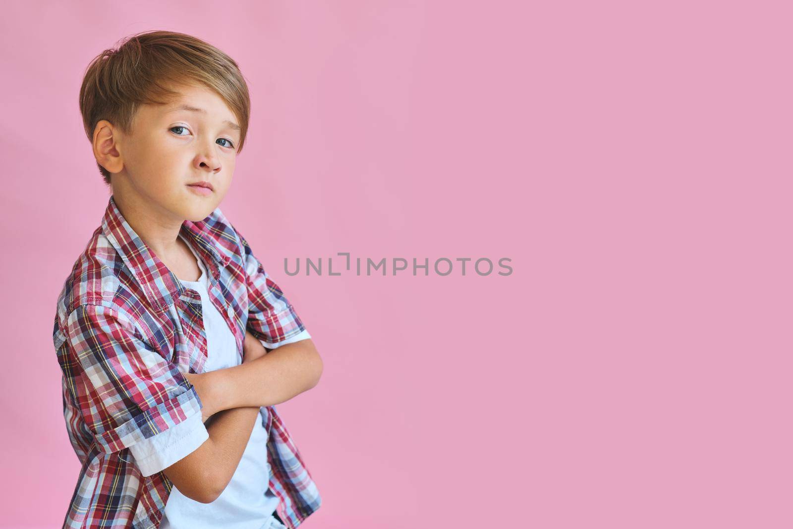 Young happy boy dressed in jeans, a white T-shirt and a plaid shirt isolated on pink background with copy space