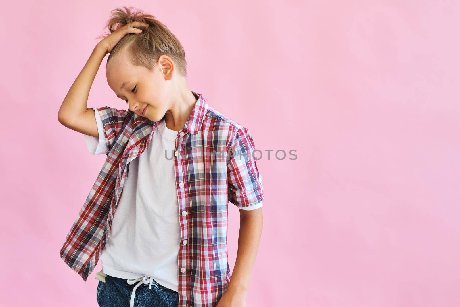 Young happy boy dressed in jeans, a white T-shirt and a plaid shirt isolated on pink background with copy space. Blank white t-shirt for your design