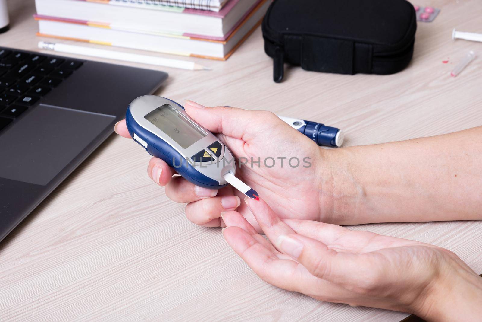 Female hands with a glucometer at the desk. The lifestyle of a person with diabetes, measuring the level of glucose in the blood.