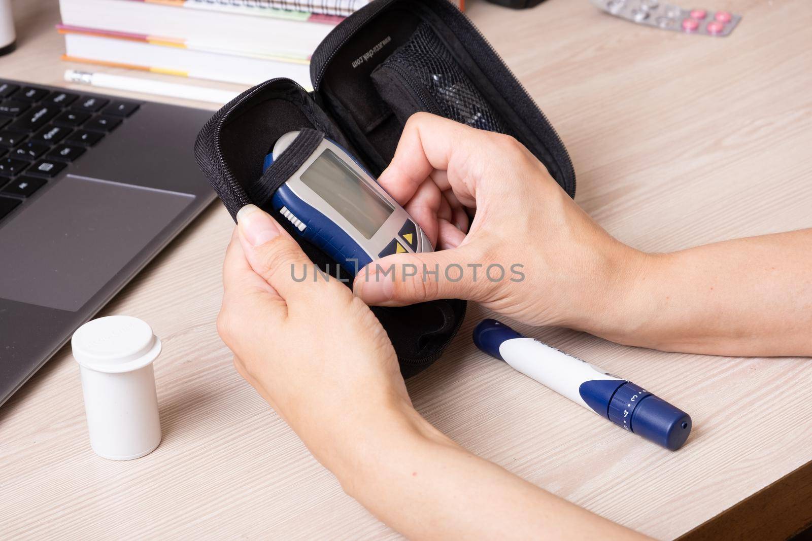 Female hands with a glucometer at the desk. The lifestyle of a person with diabetes, measuring the level of glucose in the blood.