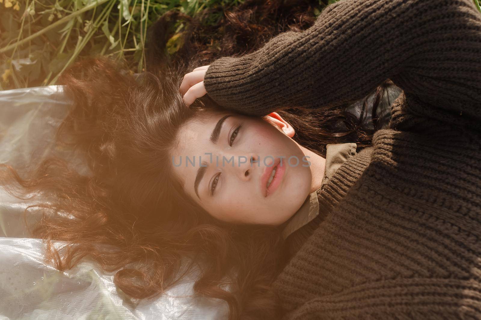 An Asian woman is lying on the ground in a field in a brown sweater. The concept of manufacturing clothing from recycled plastic. by Annu1tochka