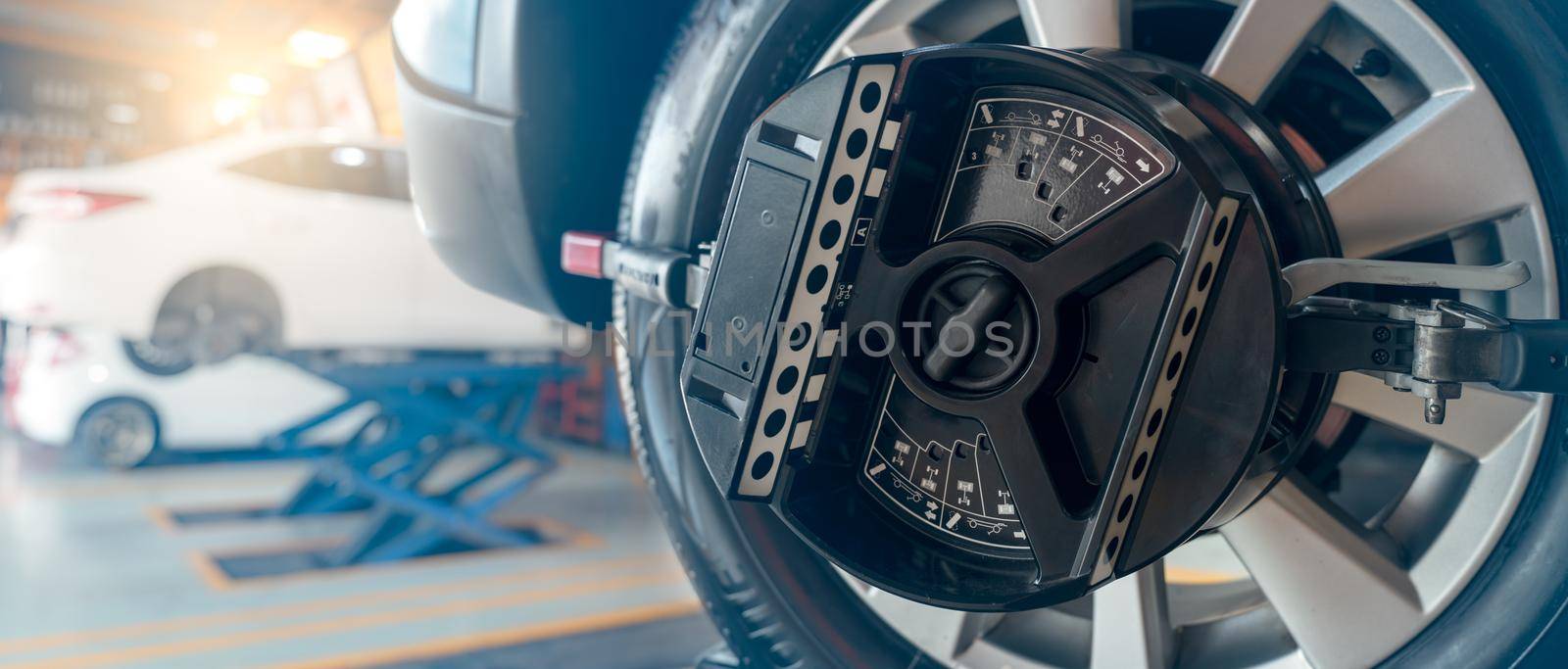 Wheel alignment equipment grip the tire of car wheel in car repair shop. Auto wheel alignment in workshop of service station. Car wheel balance. Suspension adjustment. Vehicle inside garage workshop.