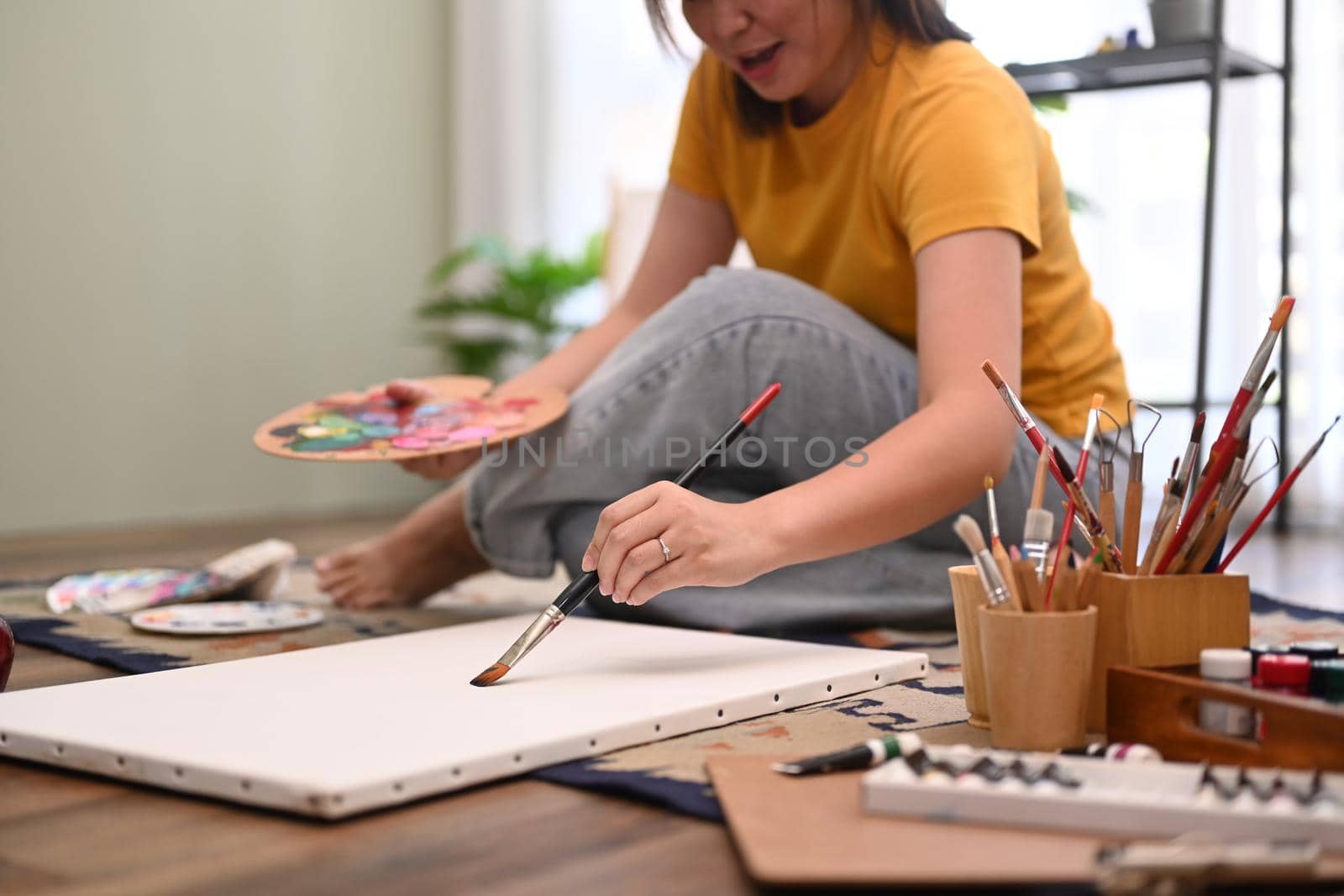Casual young woman painting art picture with watercolor on canvas, enjoy creativity activity at home. Art, hobby and leisure activity concept.