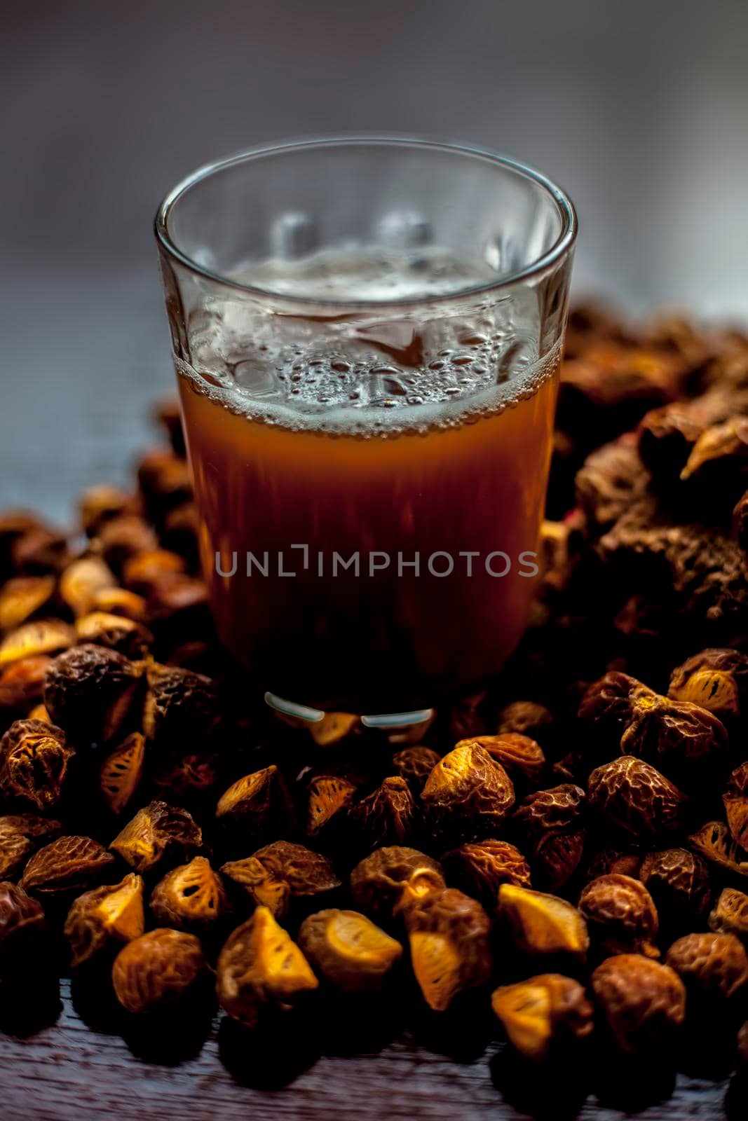 Close up shot of fresh raw soapnut on the brown surface along with its solution or liquid in a glass alongside it.