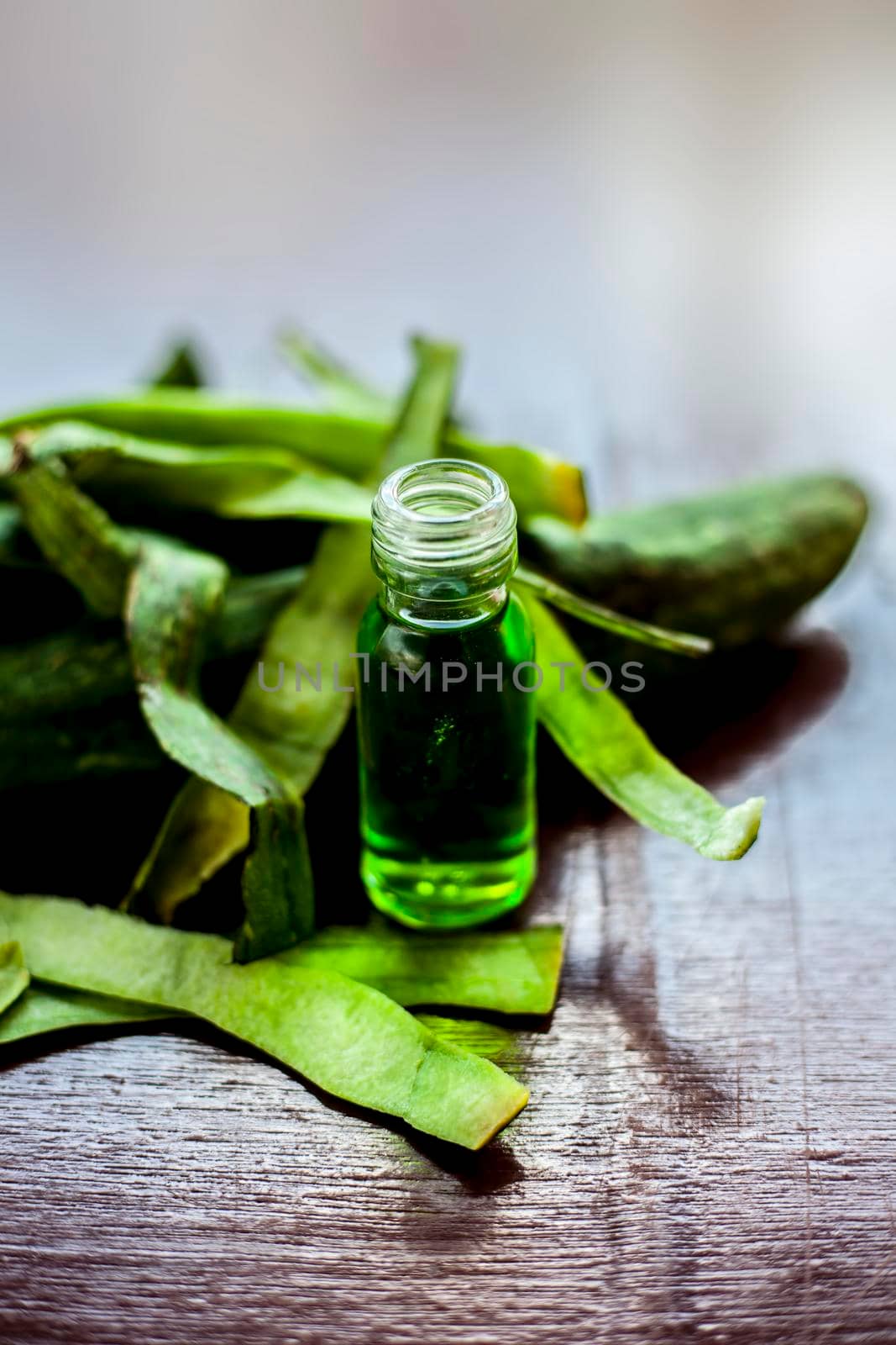 Close up shot of fresh essential oil or sponge gourd or luffa in a glass bottle along with some fresh sponge gourd on the brown surface.
