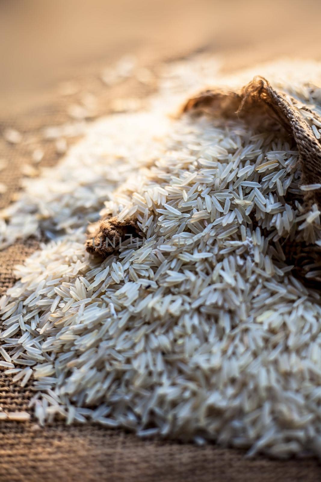 Close up shot of Raw Basmati white rice in a gunny bag on brown surface.