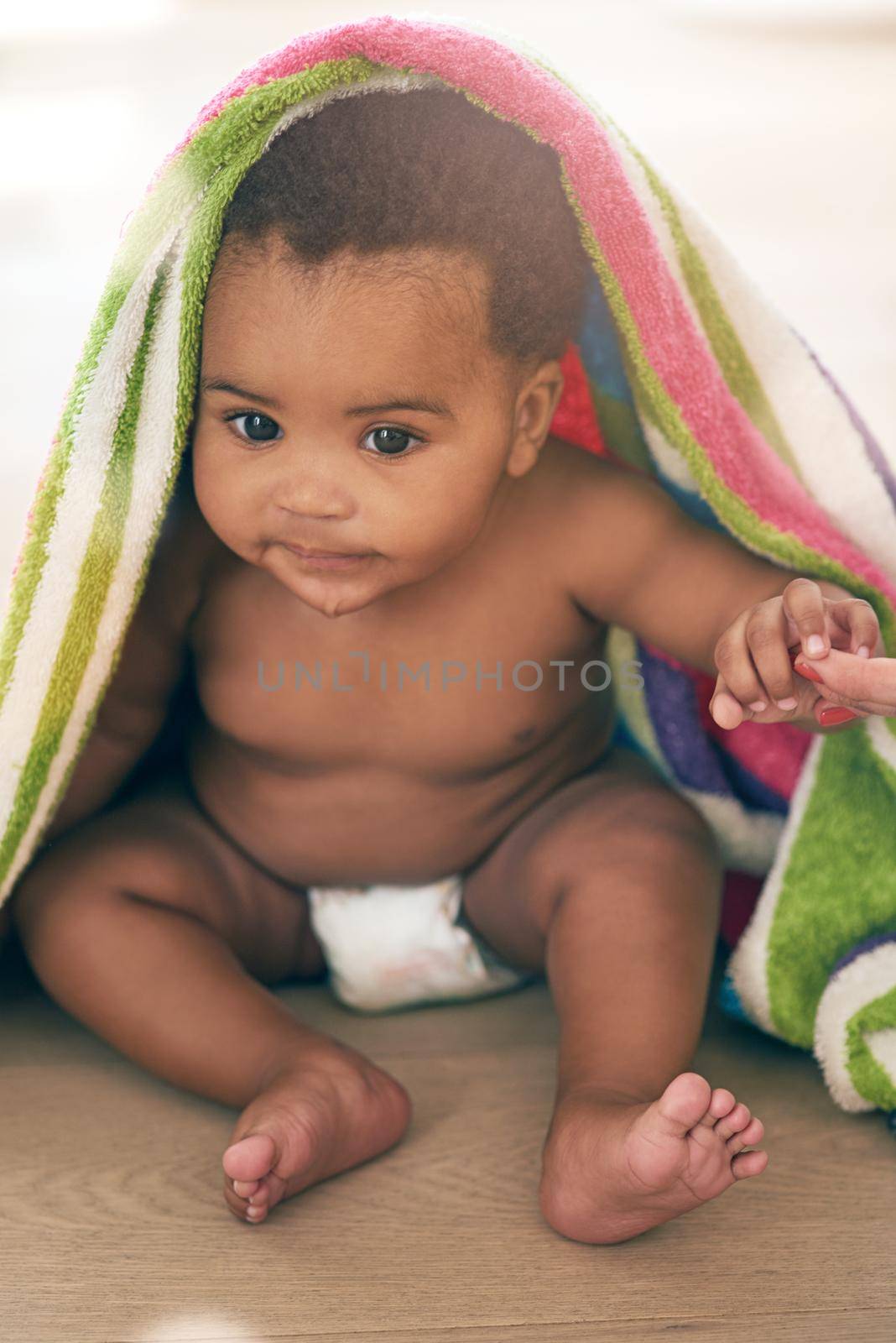 Somebody get me outta here. an adorable baby girl covered in a colorful blanket at home. by YuriArcurs
