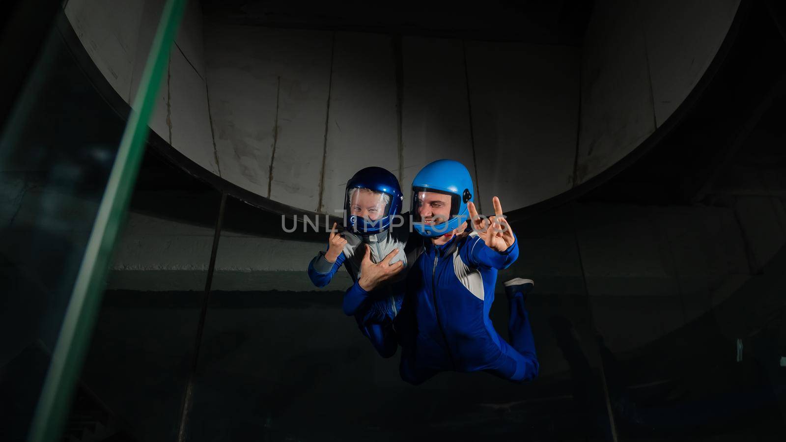 A man teaches a boy to fly in a wind tunnel. Lack of gravity