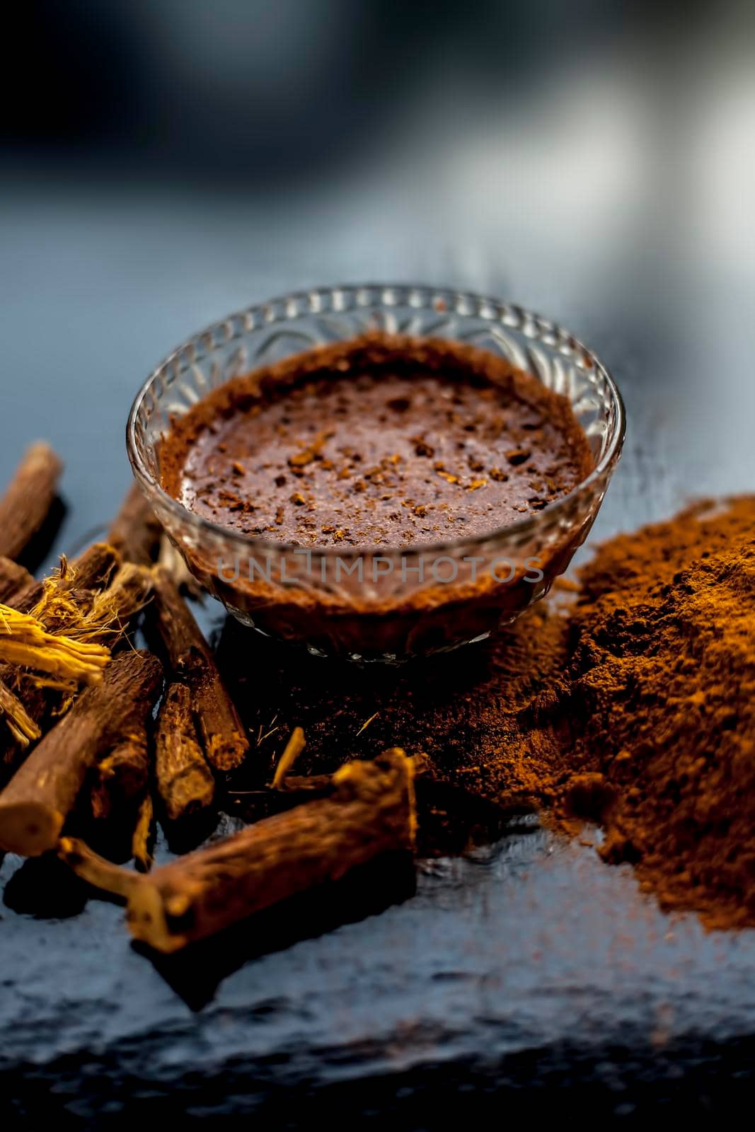 Close up shot of fresh raw revand chini roots and its paste in a glass bowl along with some raw powder on a wooden black surface.