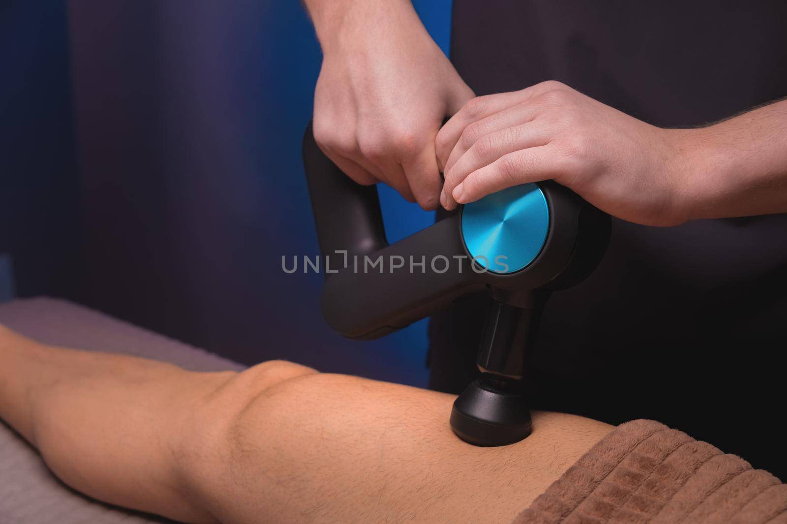 Masseur massaging legs with massage percussion device in spa center to muscular patient athlete by yanik88
