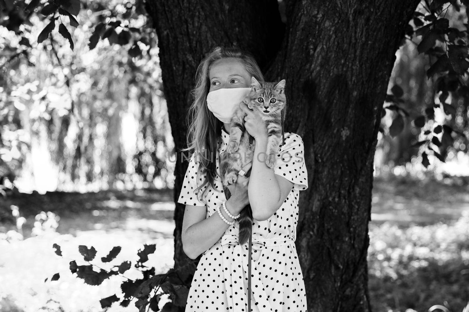 A young blonde woman in a protective medical mask holds a Scottish straight-eared kitten. A girl walks with a cat during the coronavirus kovid19 pandemic with security measures