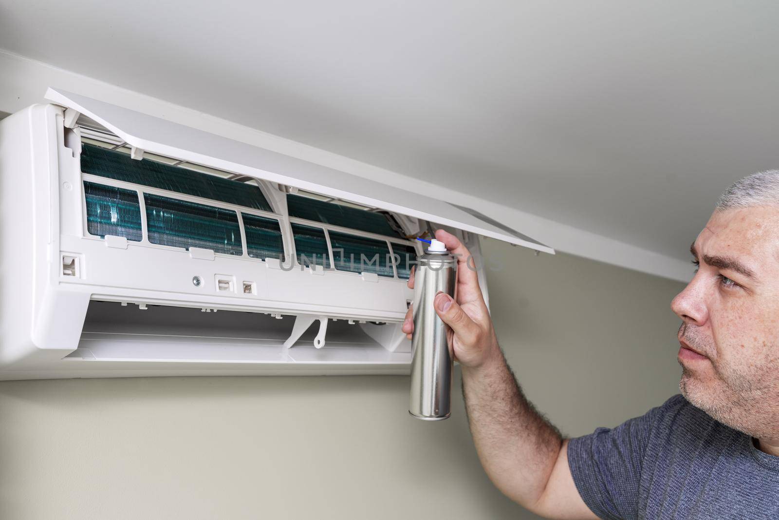man cleans the air conditioning with antibacterial spray