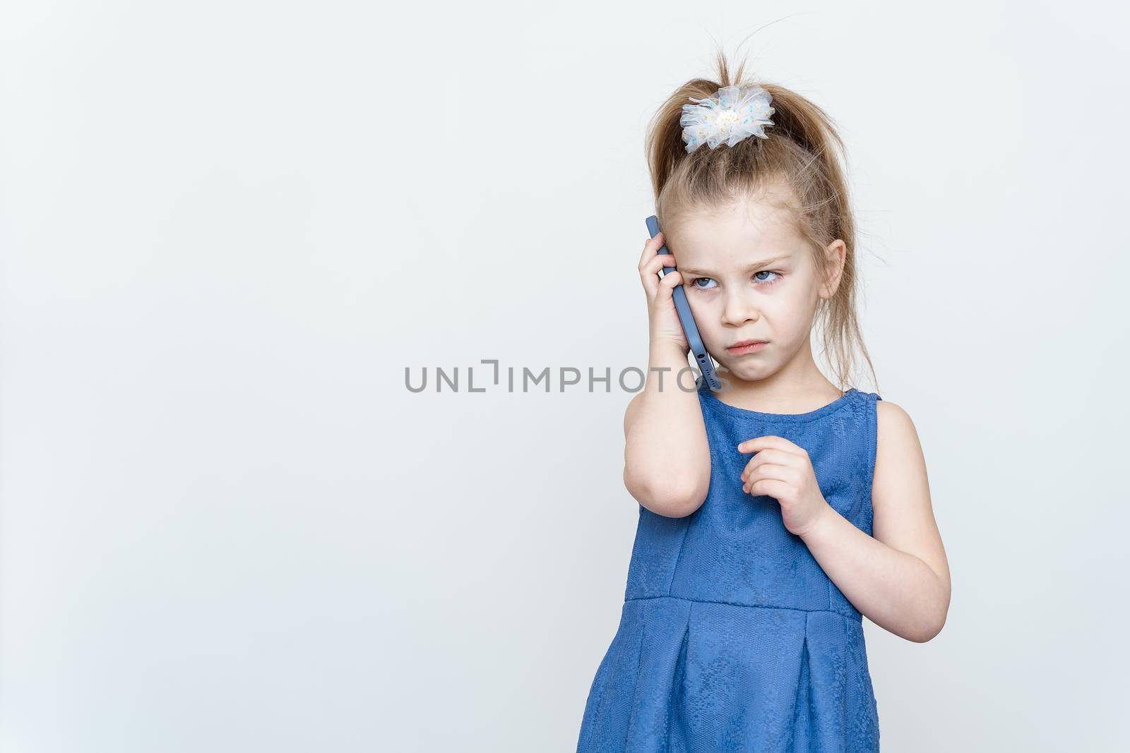 emotional 5-6 year old girl in a blue dress posing in the studio with a smartphone