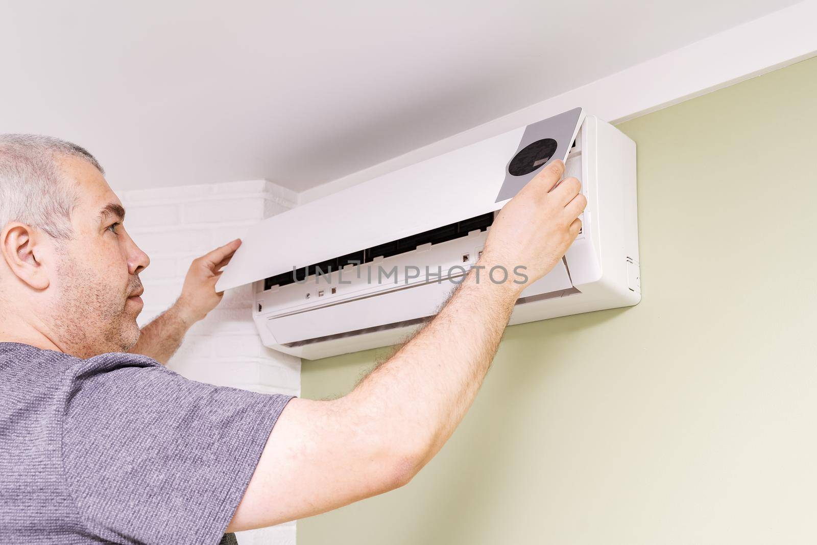 male with screwdriver in hand opens ceiling air conditioner lid in room