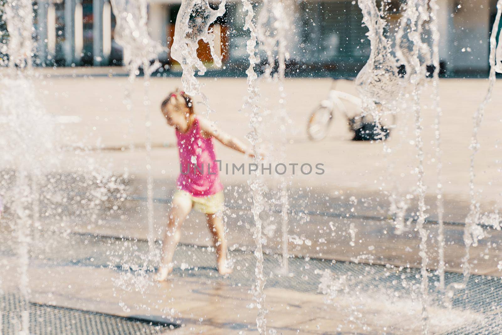 a child playing with water in a dry fountain in the city square