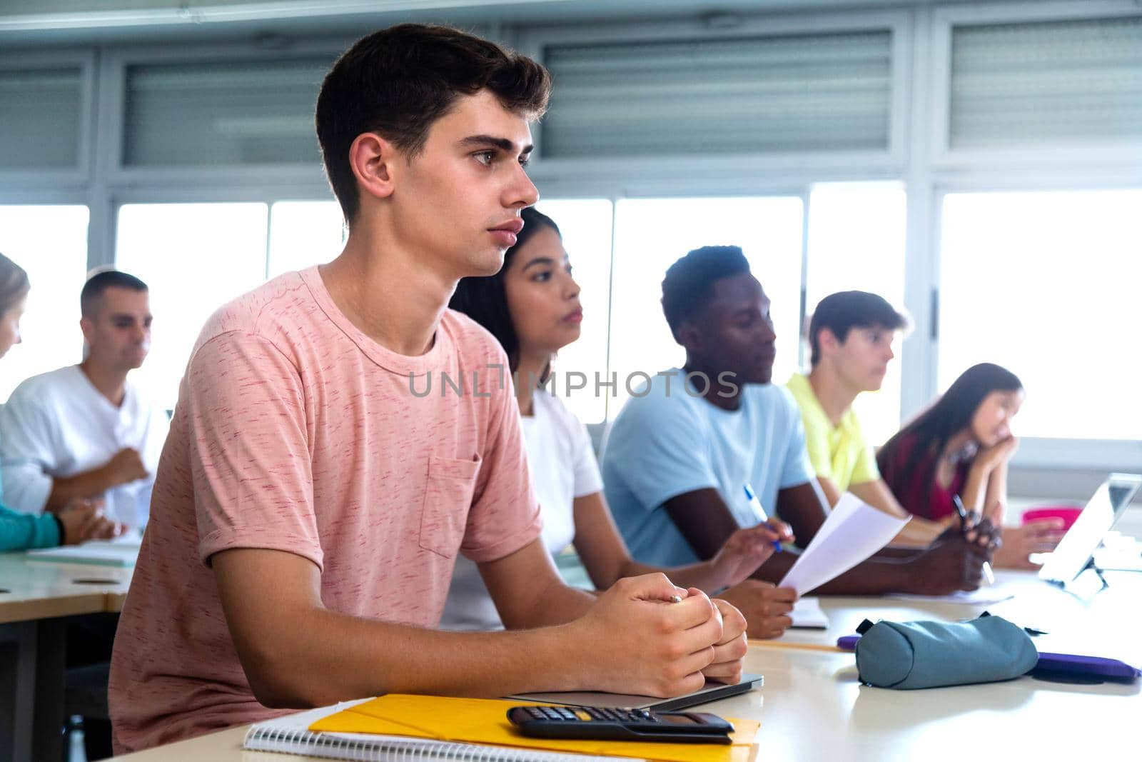 Caucasian teen male high school student in class. Multiracial university students in classroom. Copy space by Hoverstock