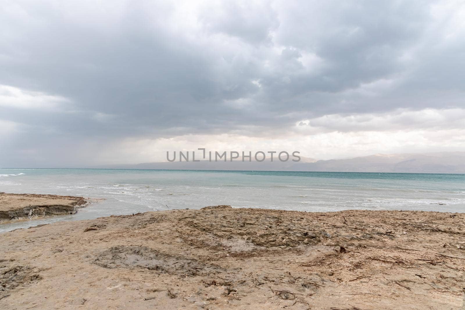 Exotic view of the sinkhole area of the Dead Sea on a stormy winter day. PhotoStorm and rain at the Dead Sea coastline. Salt crystals at sunset. The texture of the Dead sea. Salty seashore. High quality photo