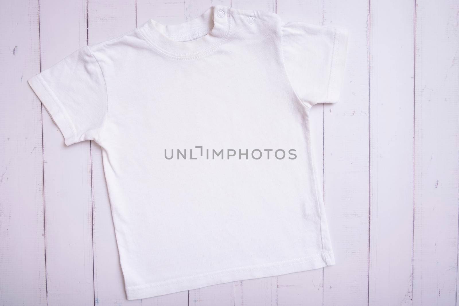 White children's t-shirt mockup for logo, text or design on wooden background top view.