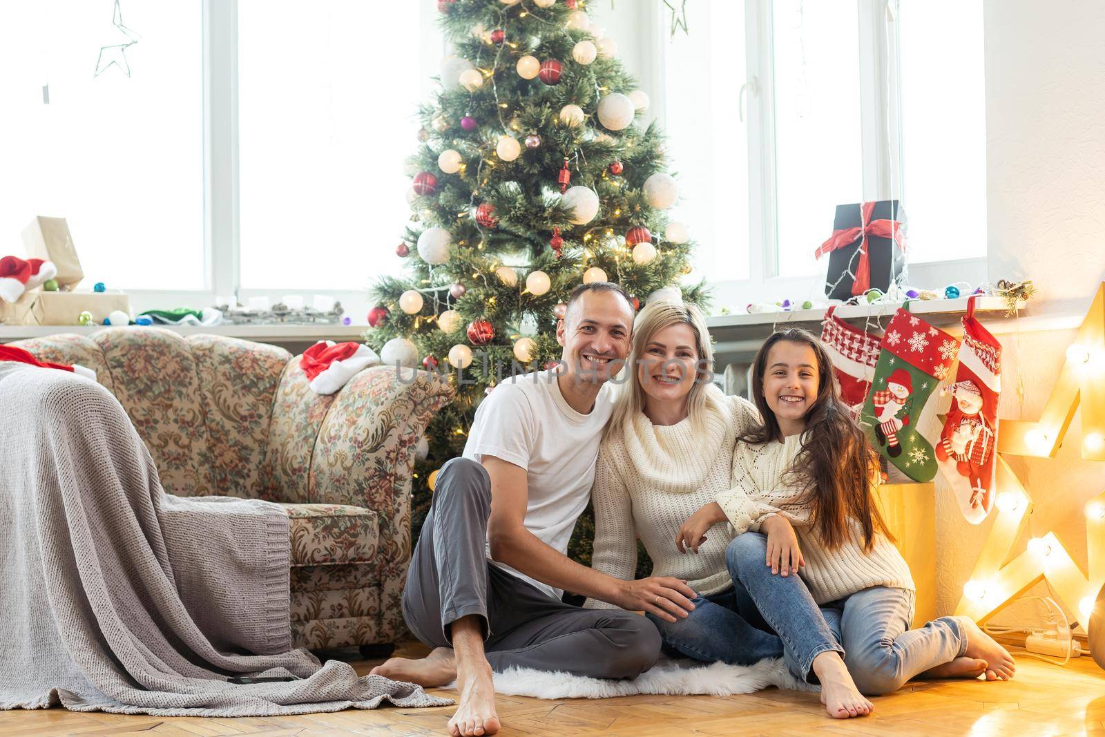 Beautiful young family enjoying their holiday time together, decorating Christmas tree, arranging the christmas lights and having fun